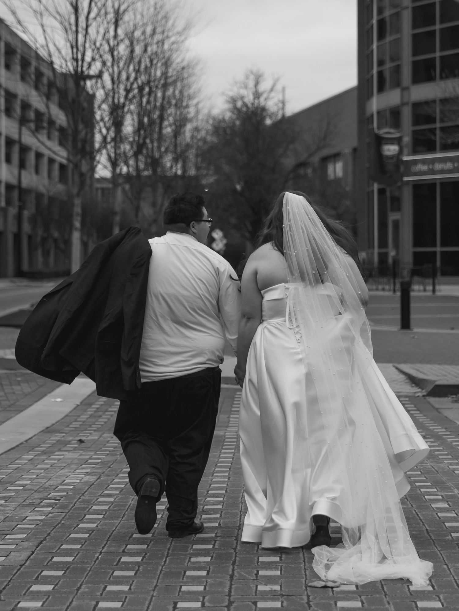 Newlyweds walking together on brick pavement with architectural buildings in background.