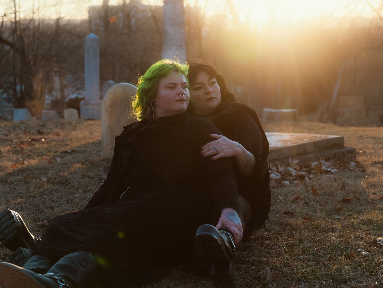 Two people rest together on the ground during golden hour as sunlight creates a warm glow in the background.