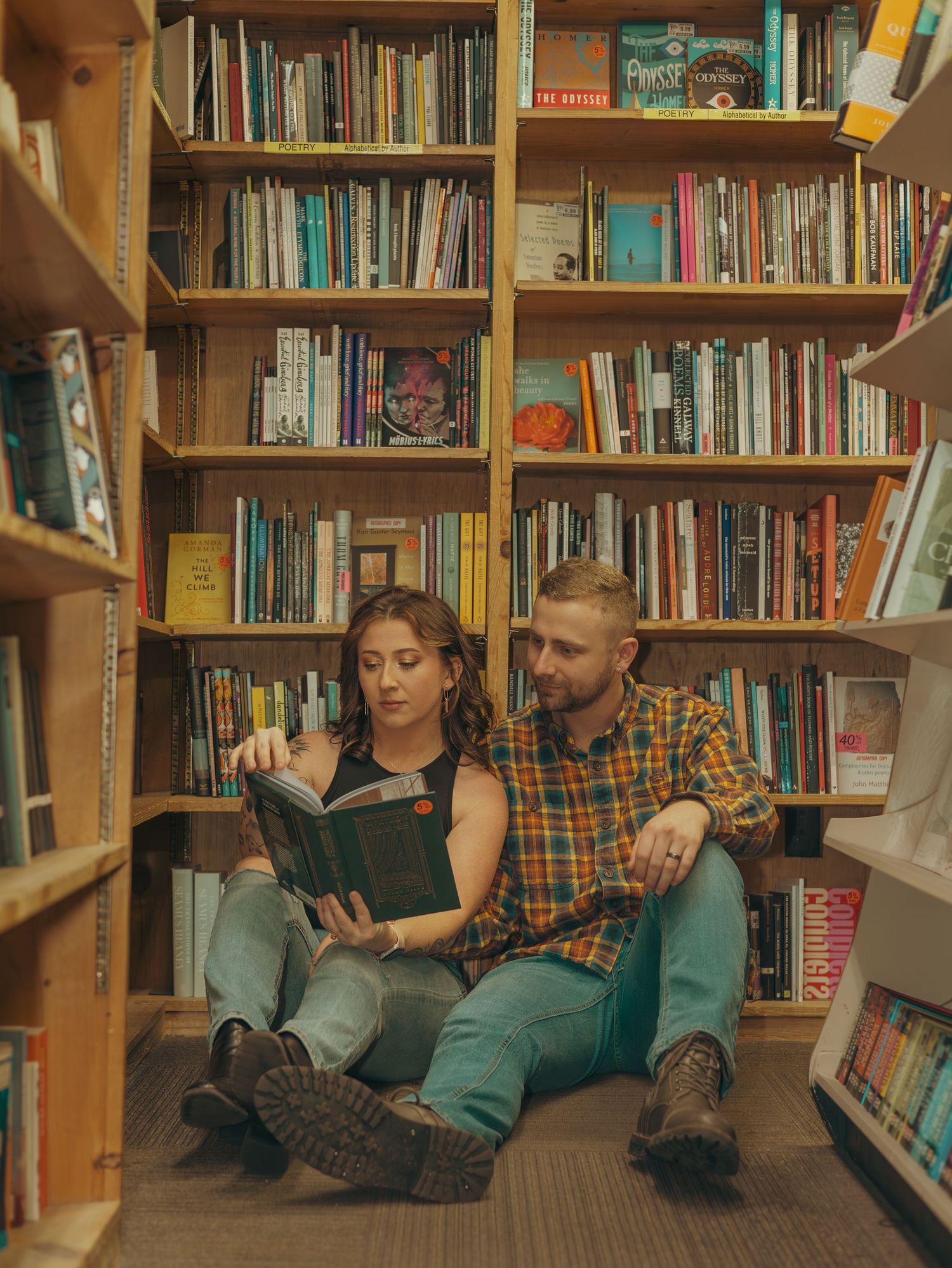 Two people sit together reading books in a cozy library corner surrounded by wooden bookshelves.