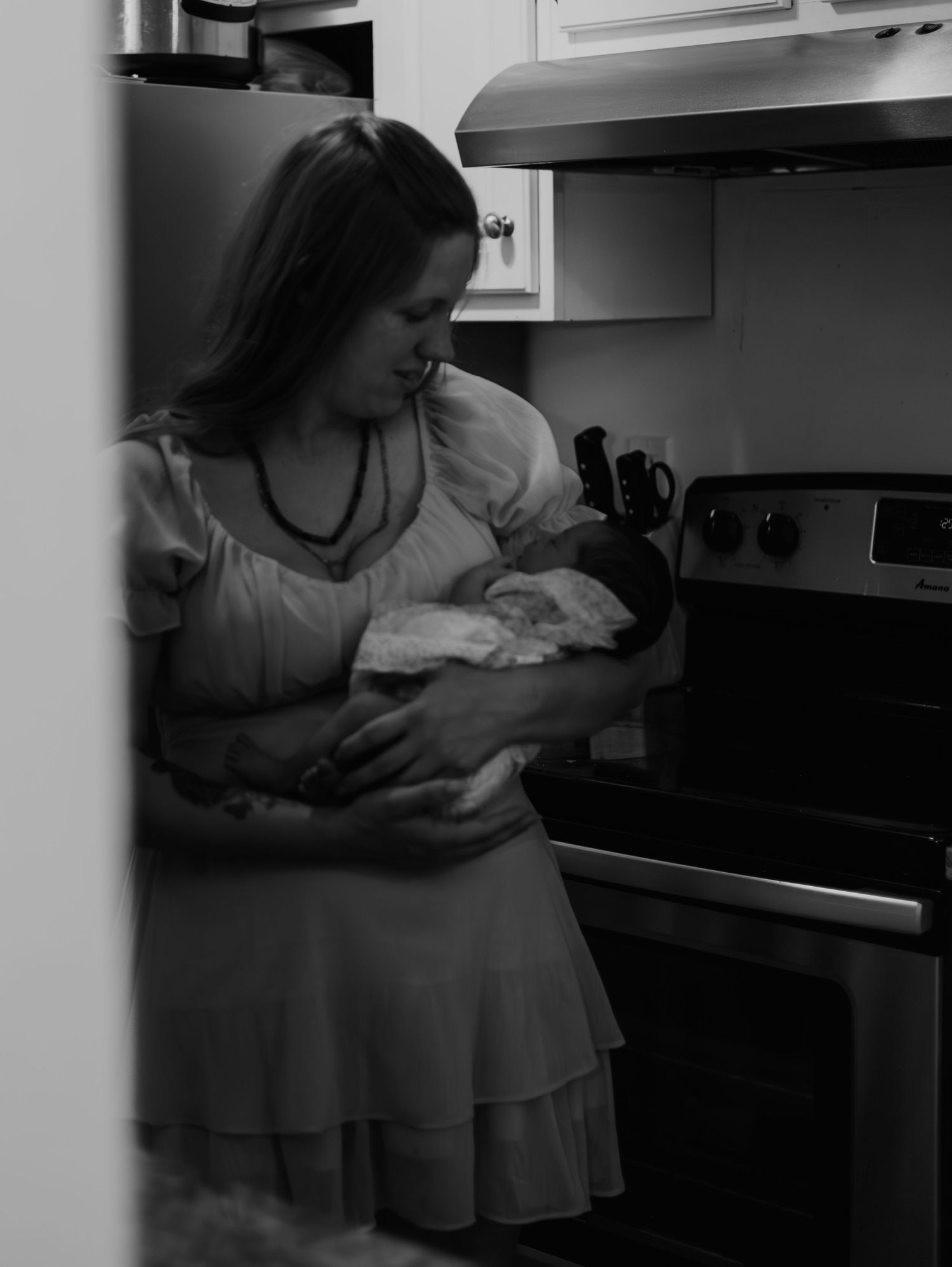 A person in a white dress bends down to check an oven in a modern kitchen.