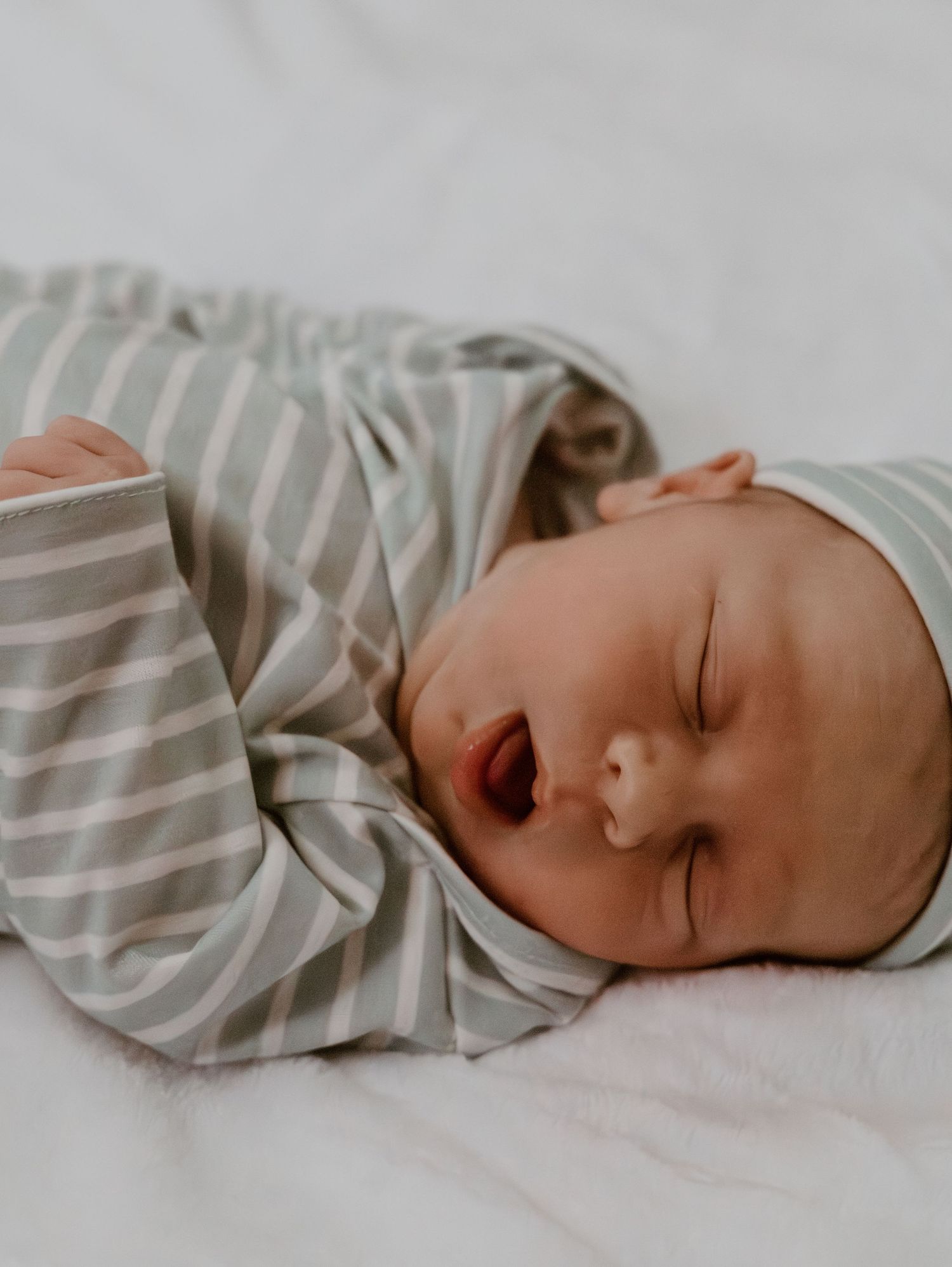 Newborn baby sleeping peacefully in sage green striped pajamas on a white blanket.