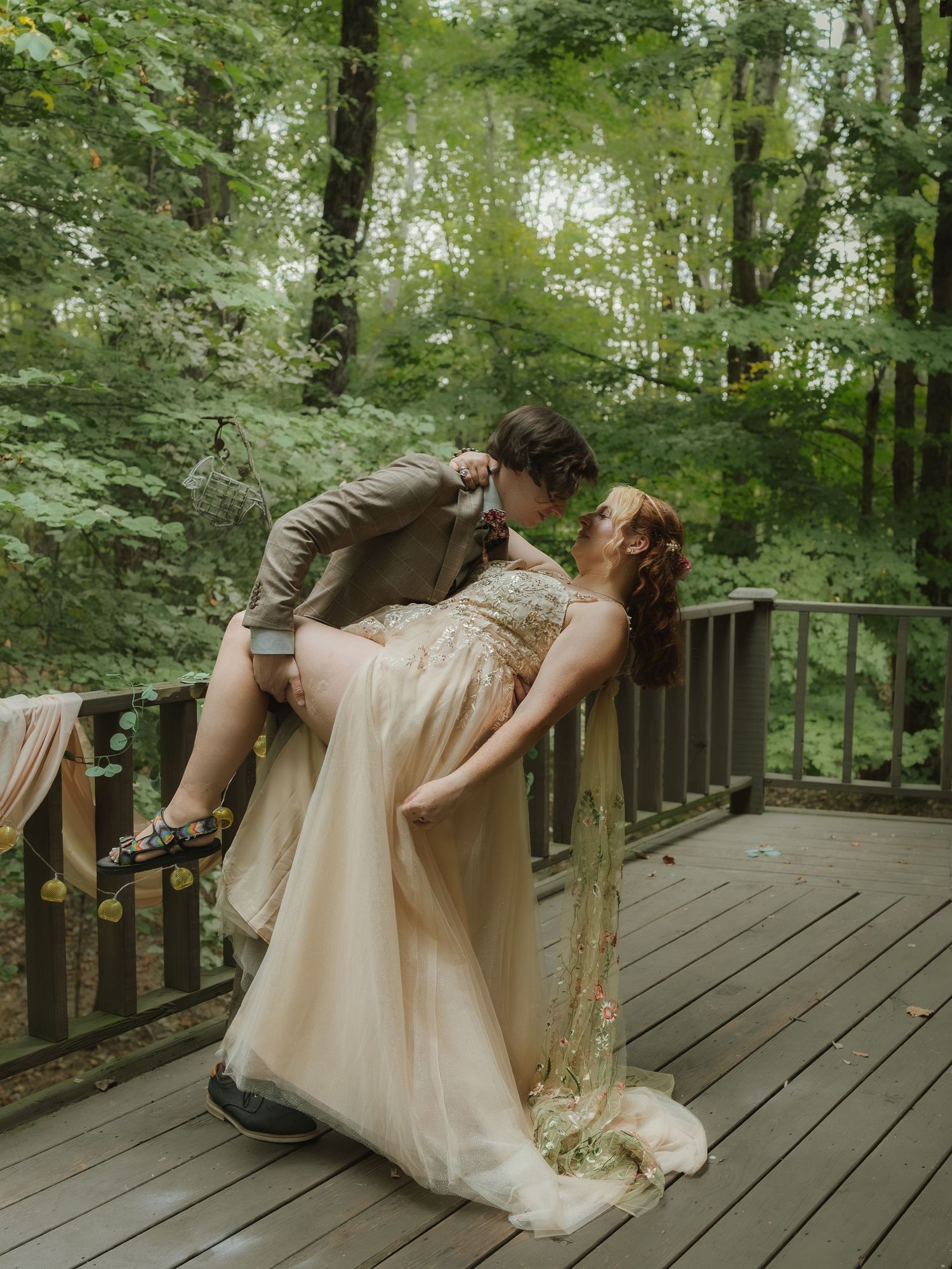 Couple sharing a romantic dip pose on a wooden deck surrounded by lush forest.