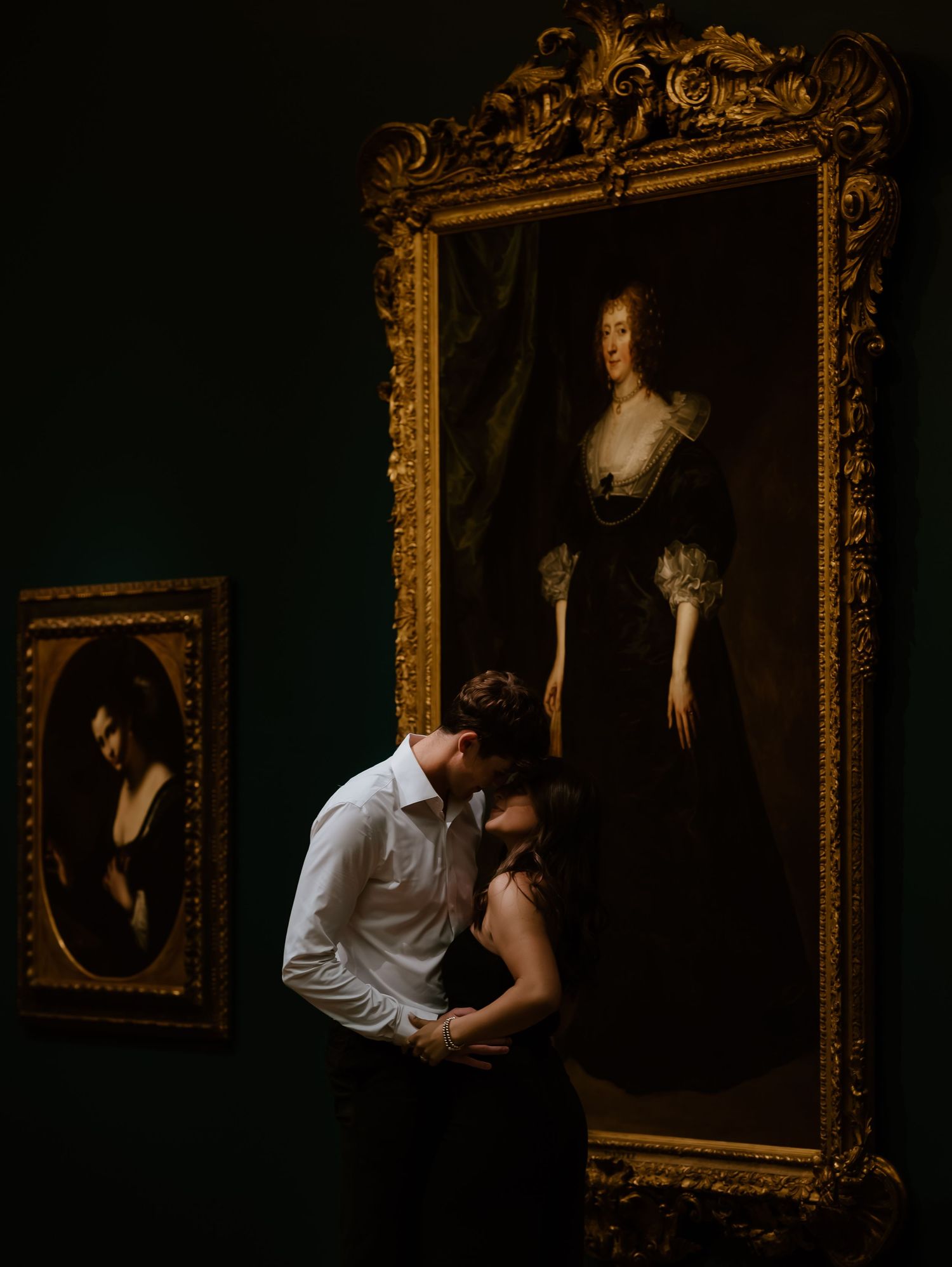 A series of vintage portraits in ornate gold frames hang on a dark wall in an art gallery setting.