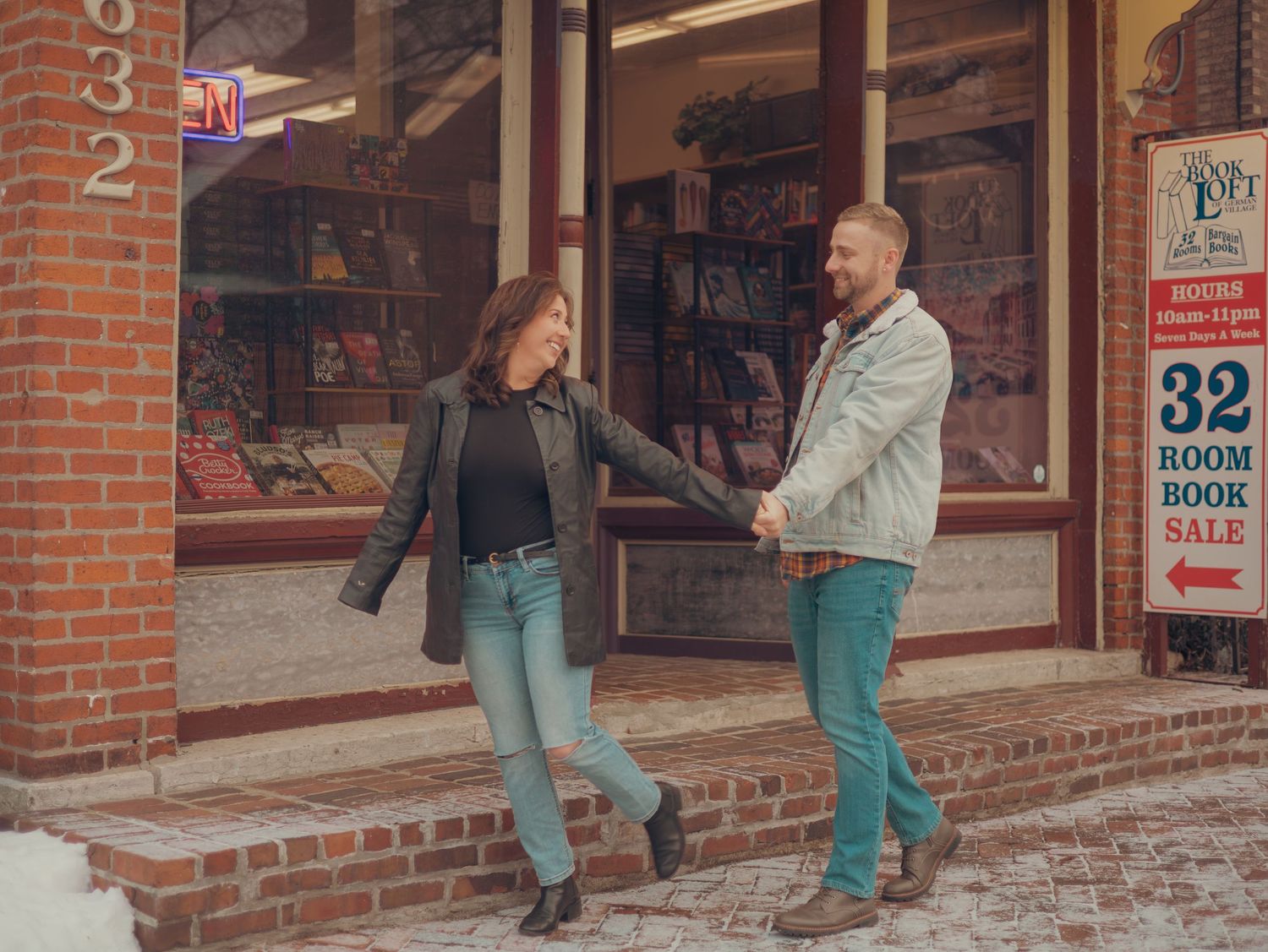 A couple laughs together while standing outside a vintage bookstore with brick walls and display windows.