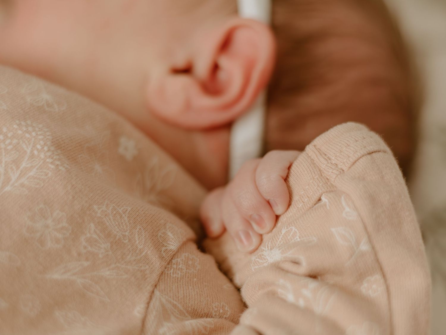 Close-up view of a newborn baby's ear and soft skin against light pink fabric.