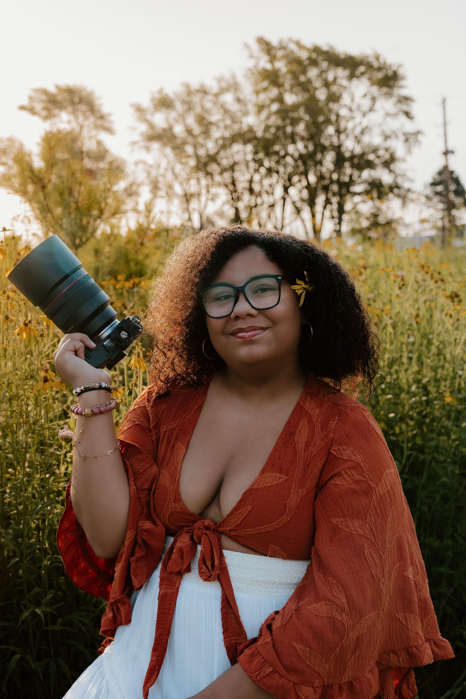 A person in a rust-colored jacket and glasses holds a reusable coffee cup against an autumn outdoor background.