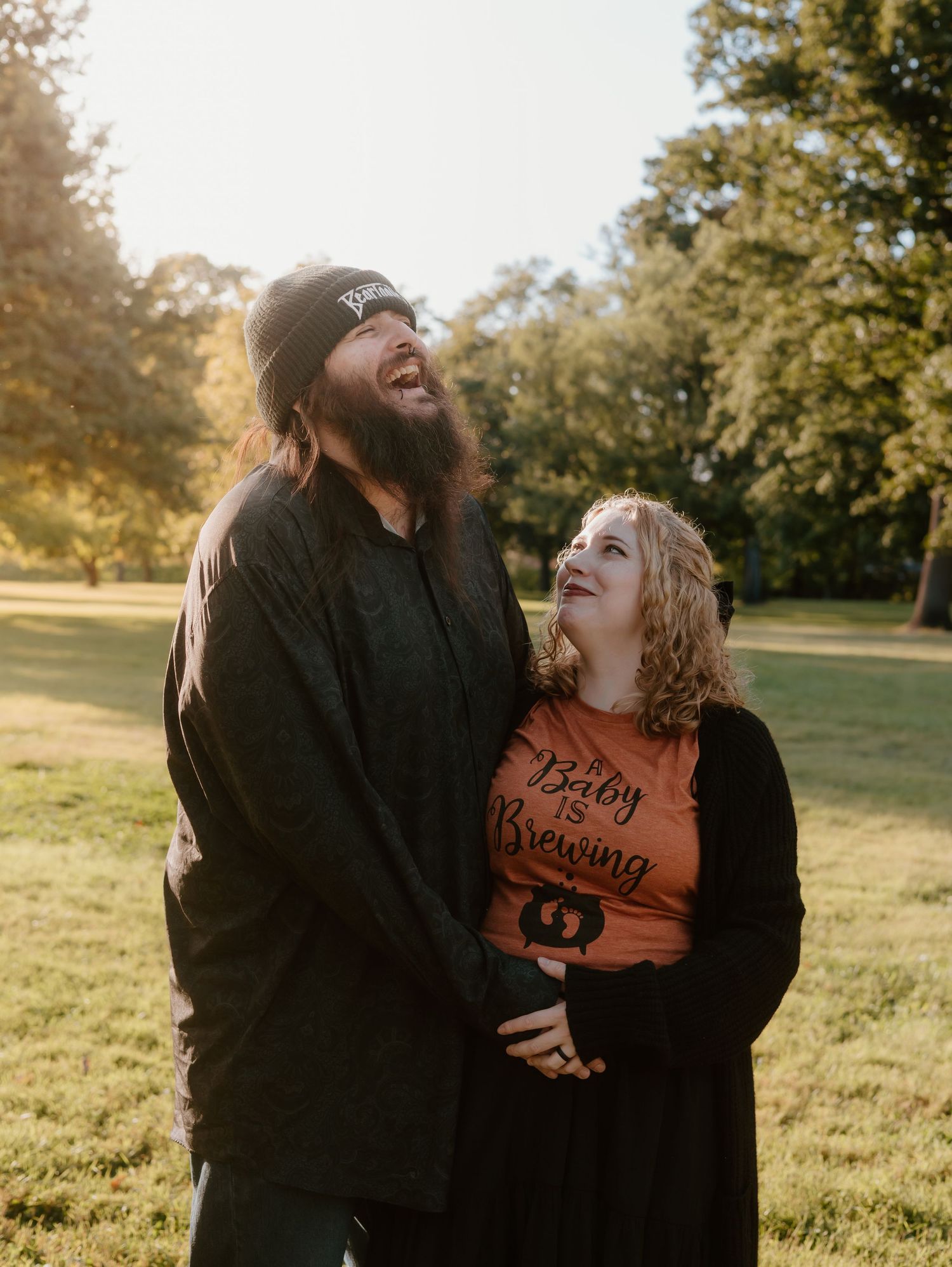 A couple shares intimate moments in a park during golden hour wearing casual attire.