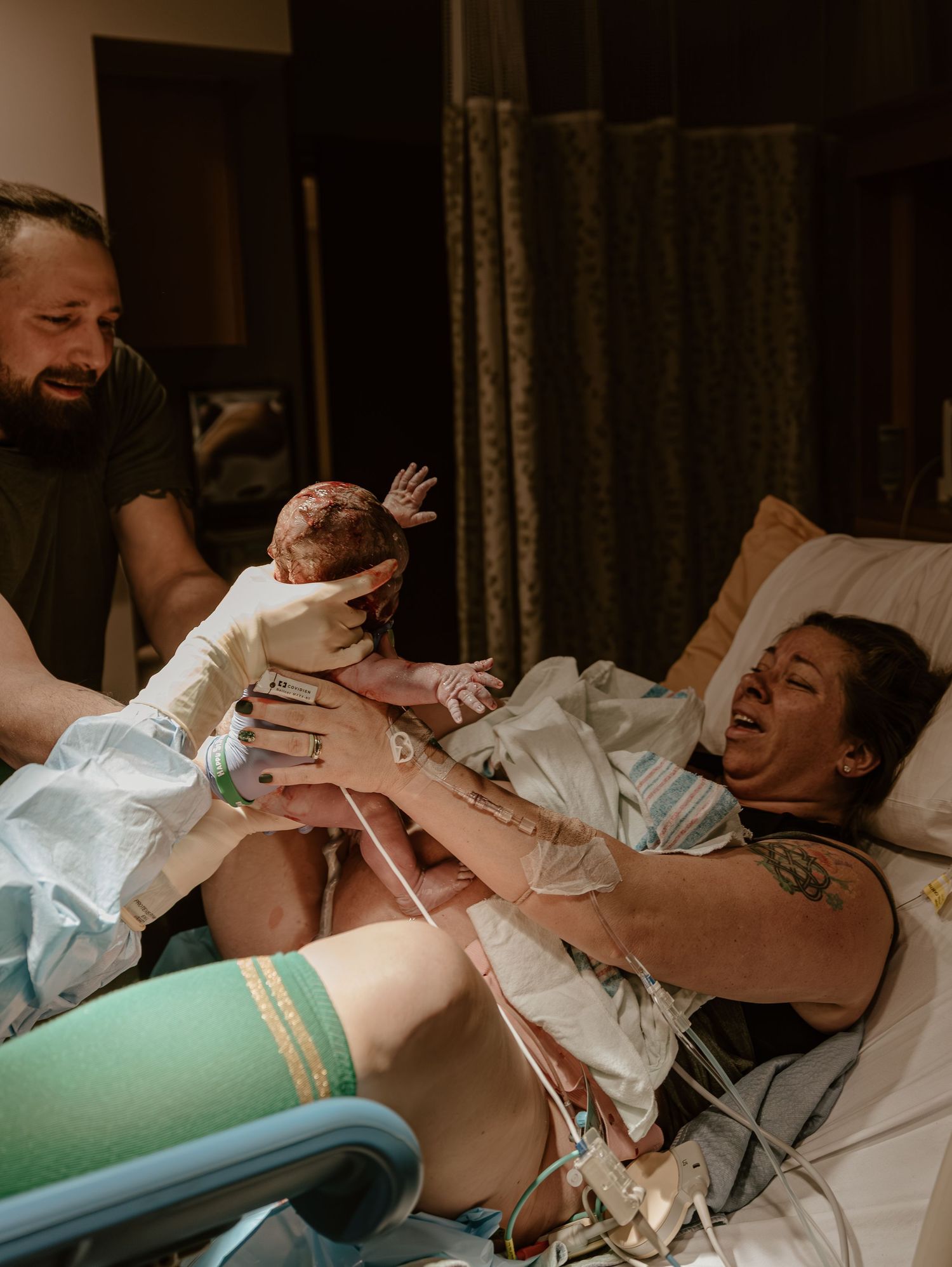 A newborn baby being held up during childbirth in a hospital delivery room with medical staff assisting.