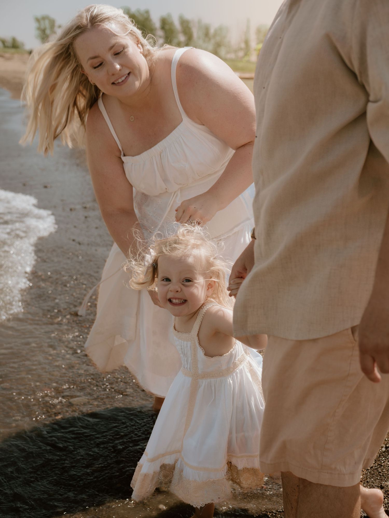A joyful moment captured on a beach with people in white outfits laughing together by the water.