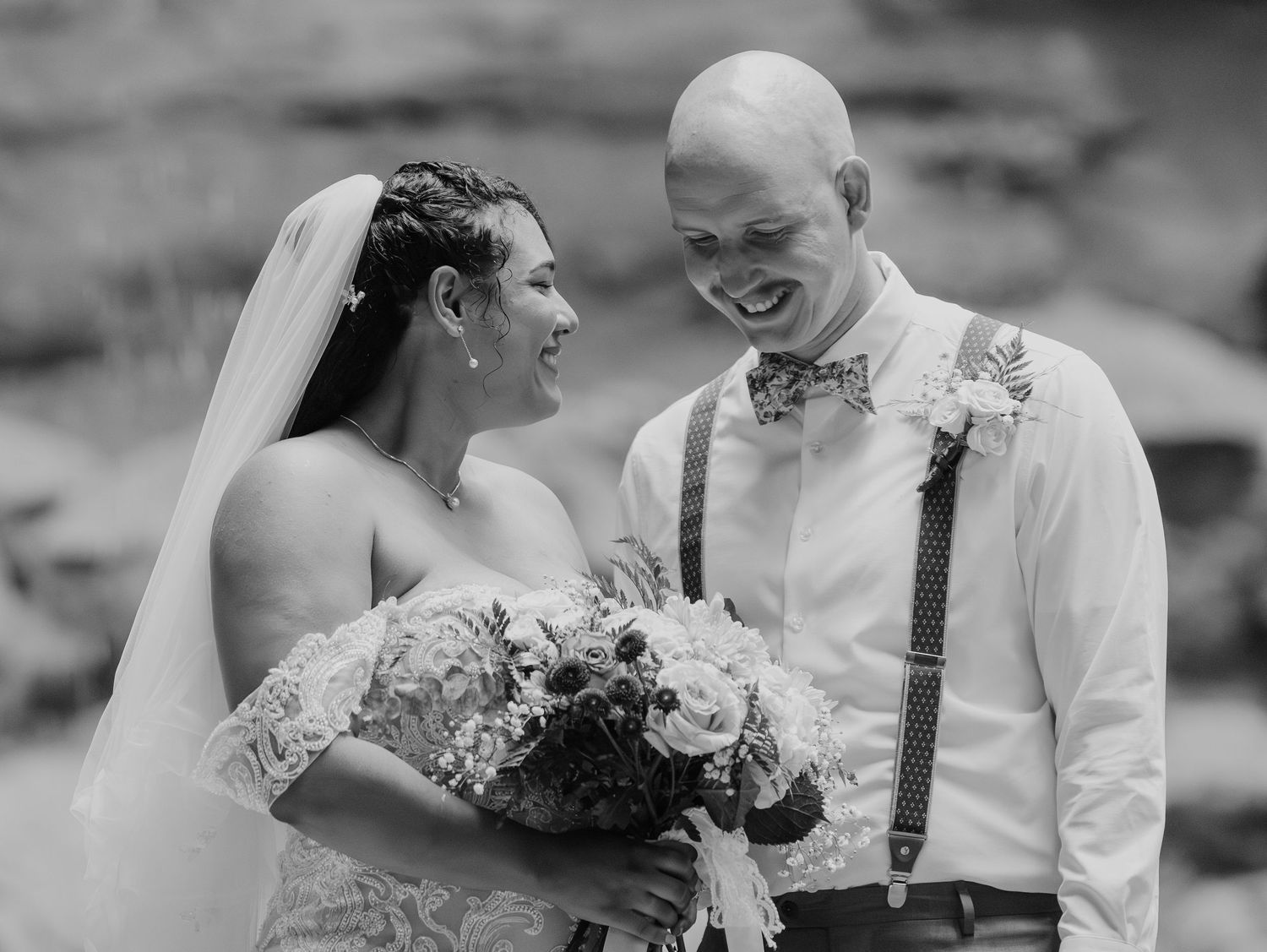 A joyful black and white wedding photo showing a couple sharing a candid moment with flowers.