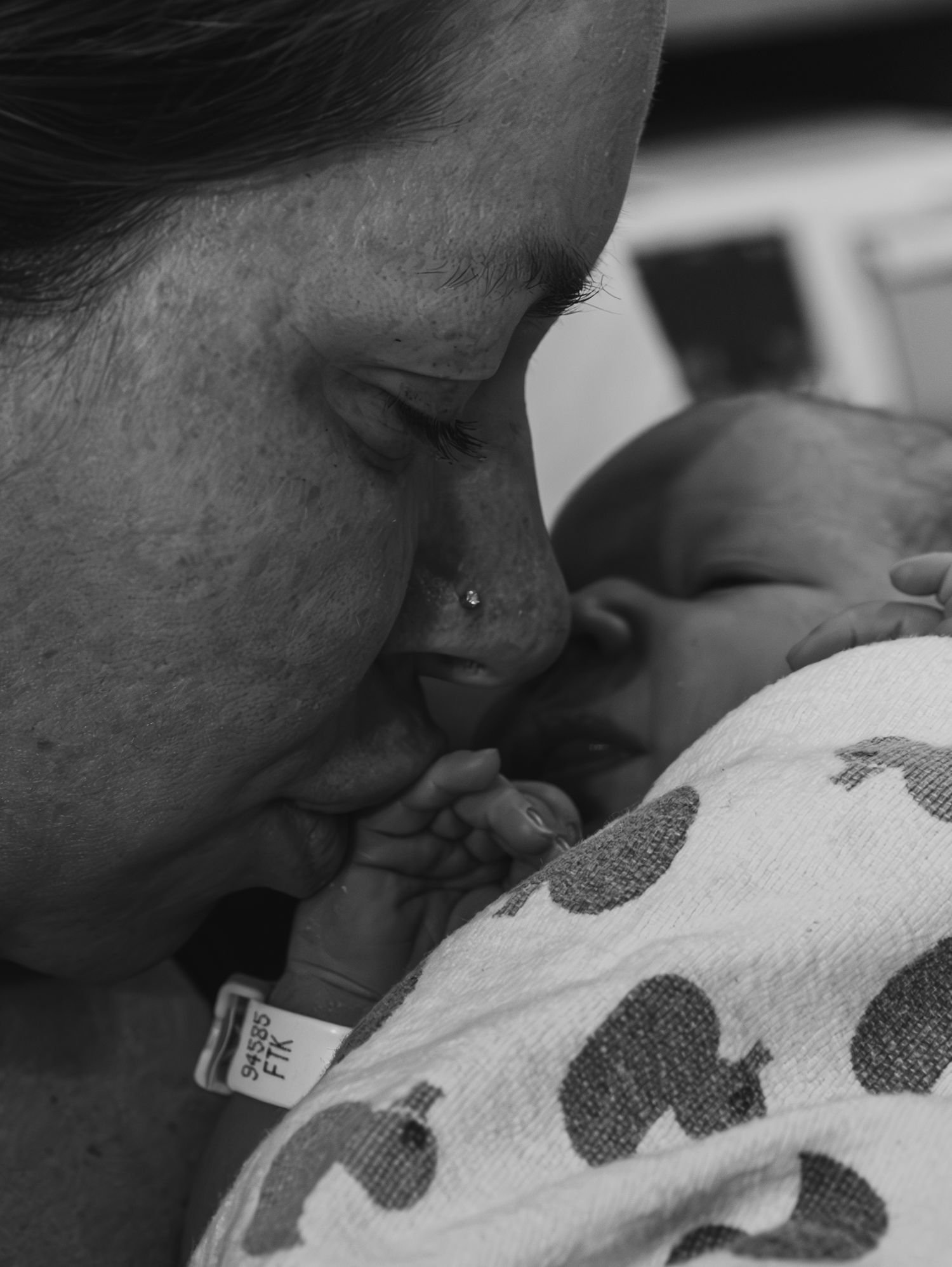 A tender black and white photograph showing a close embrace between a caregiver and a baby wrapped in polka dot blanket.