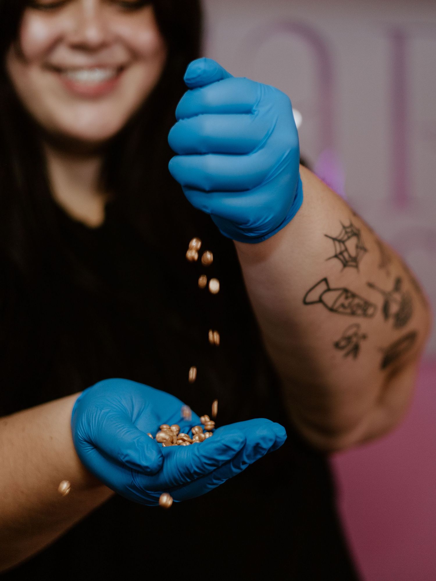 Someone wearing blue medical gloves sprinkles small food items between their hands, showing a tattooed forearm.