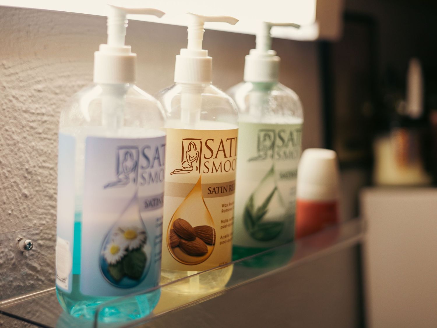 Bottles of liquid soap or shampoo lined up on a white bathroom shelf with soft focus creating a gradient effect.