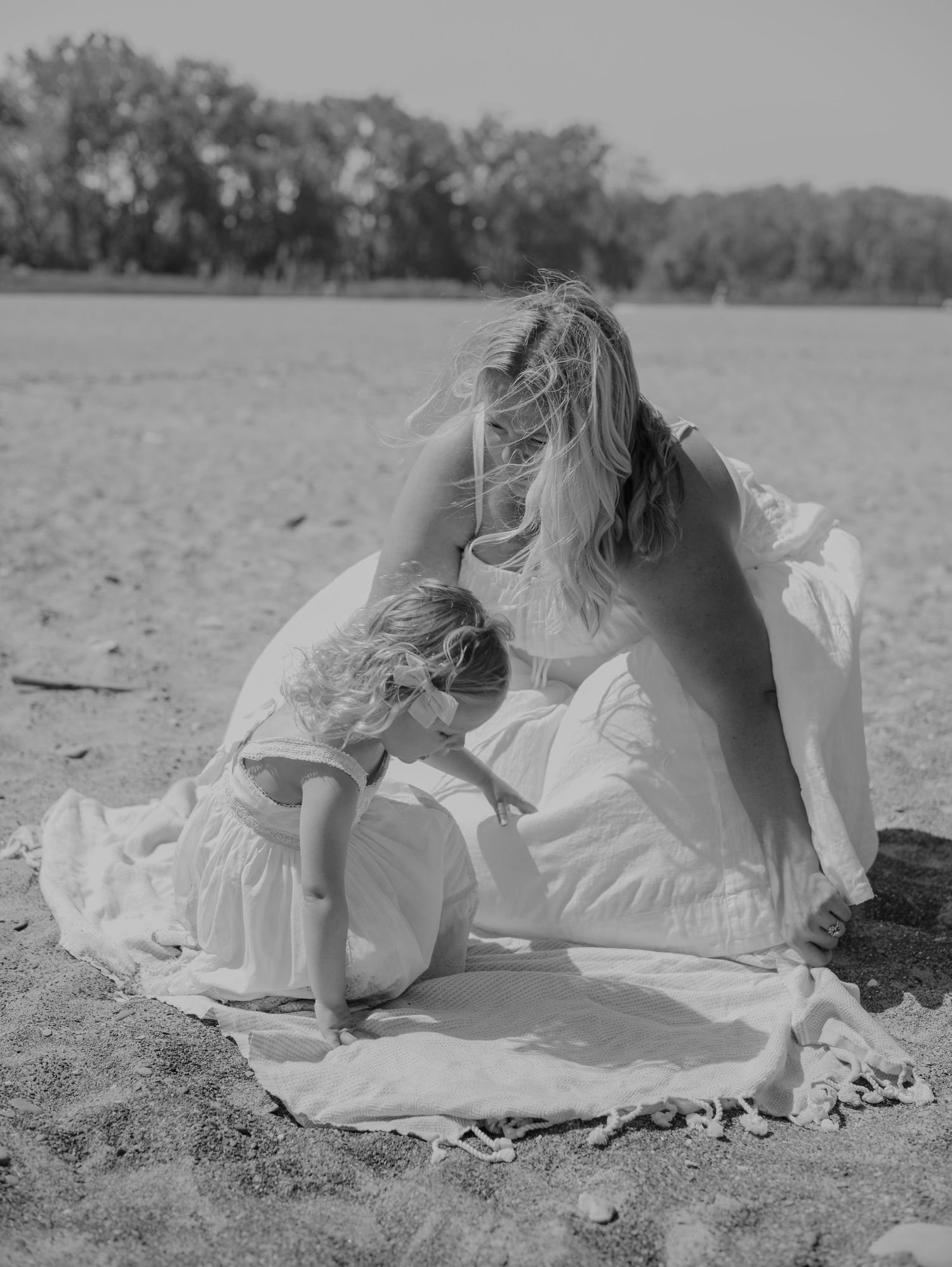 A figure in white clothing lies on a sandy beach, creating a dreamy black and white composition.