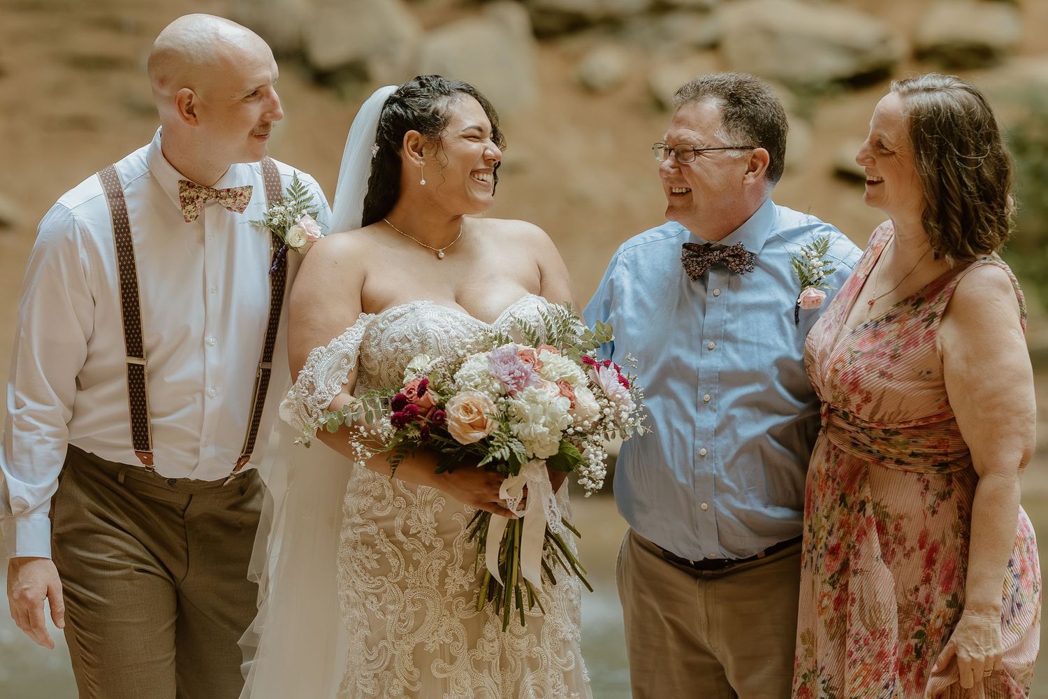Wedding party of four posing outdoors with the bride holding a beautiful floral bouquet.