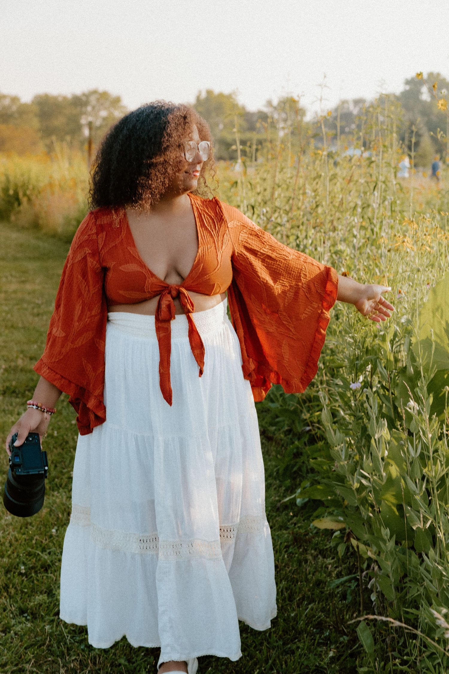 A dreamy autumn scene with a flowing white dress and burnt orange jacket amid tall wildflowers.