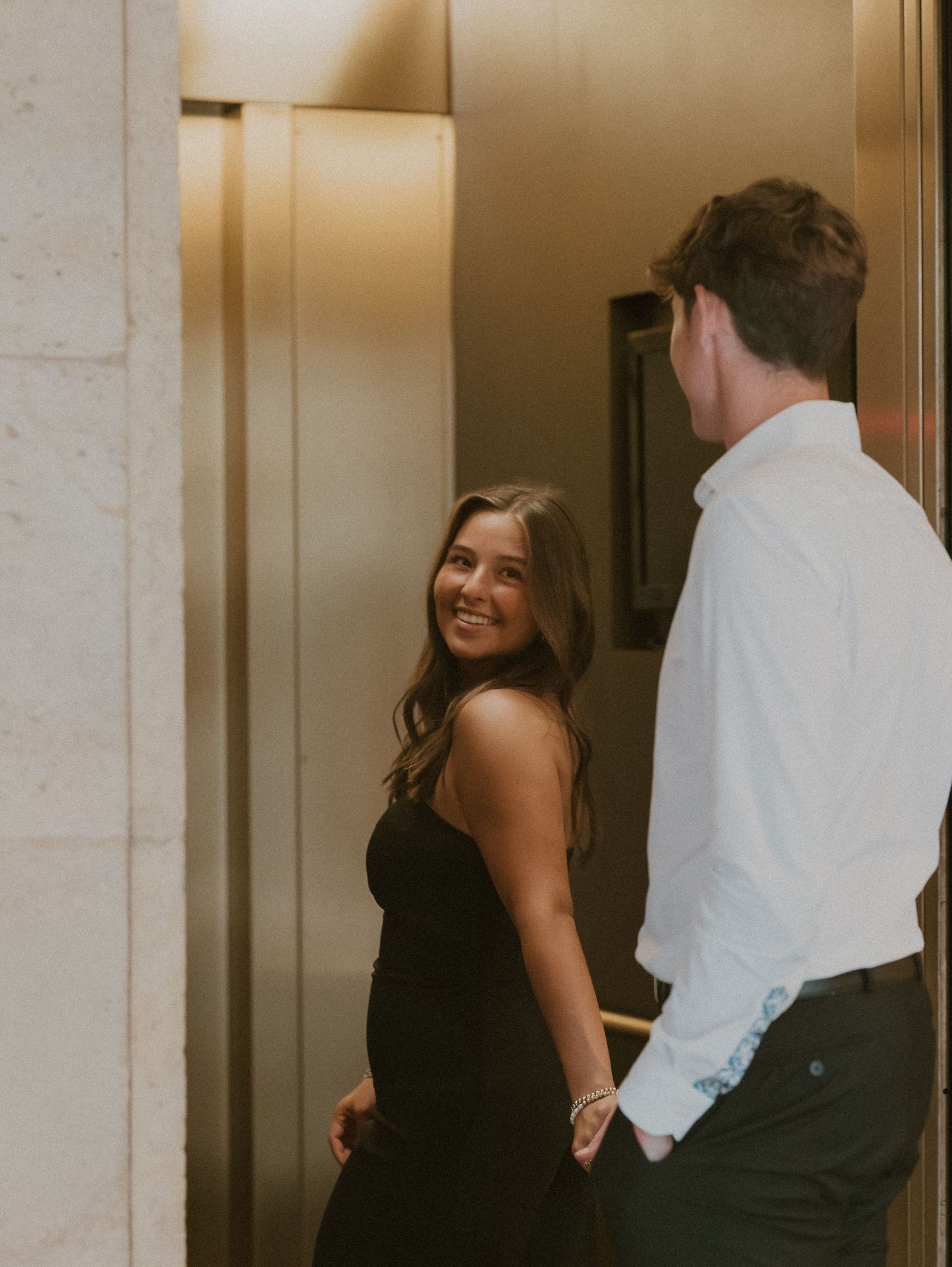 A couple shares a lighthearted moment in a warmly lit corridor.