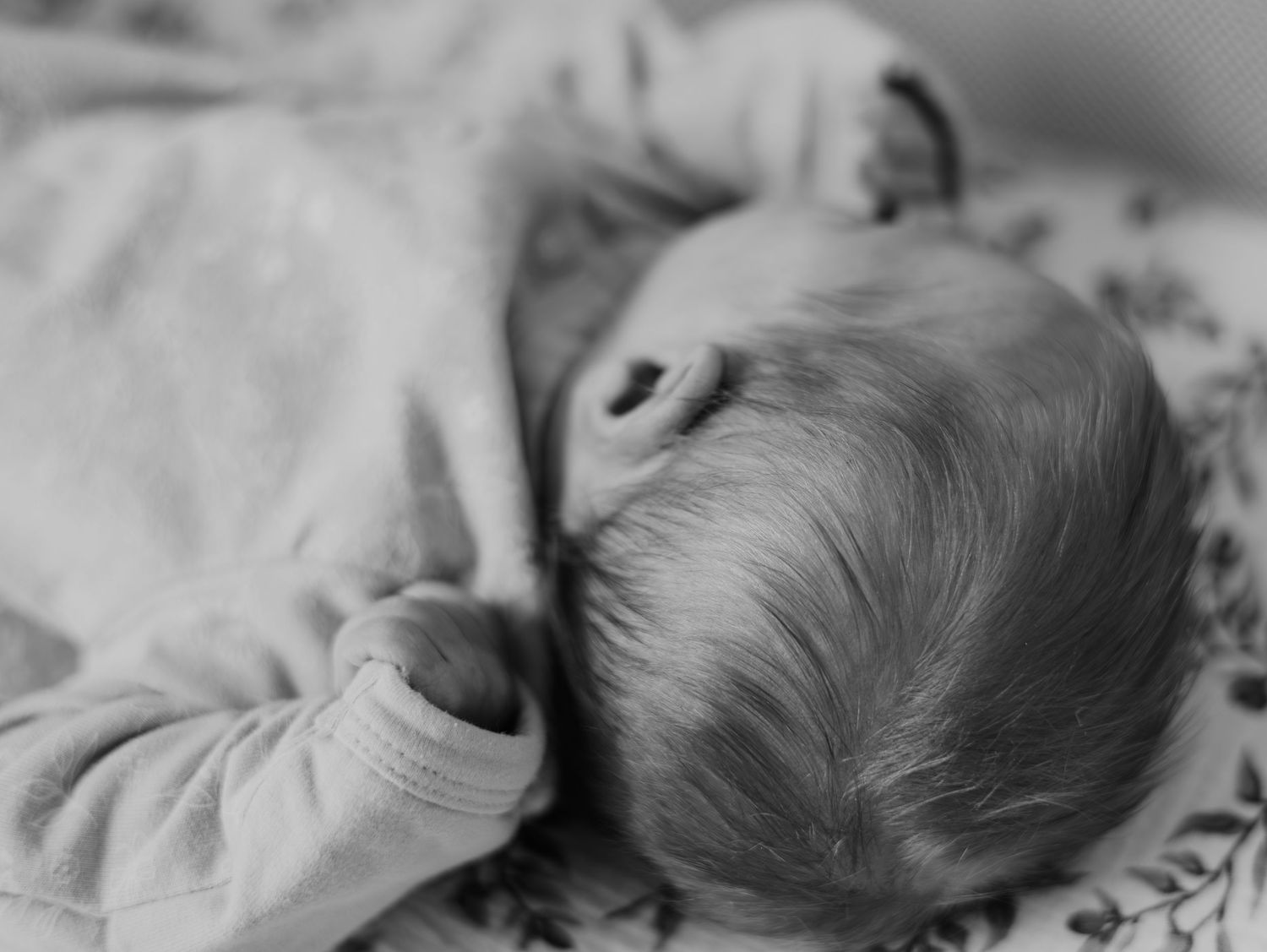 A black and white close-up photograph of a sleeping baby lying on patterned bedding.