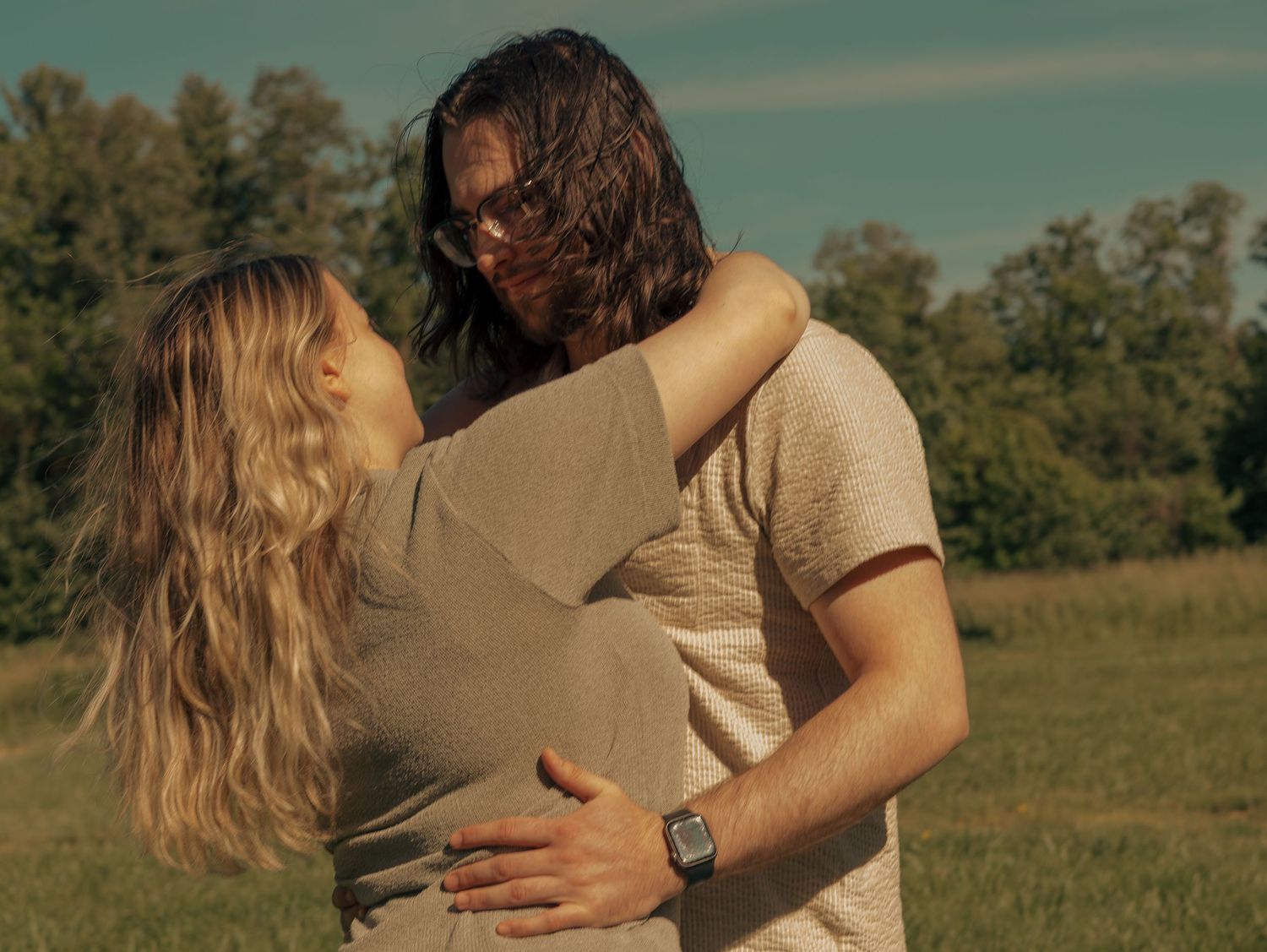 A romantic couple embraces in a sun-drenched meadow during golden hour, creating a dreamy outdoor moment.