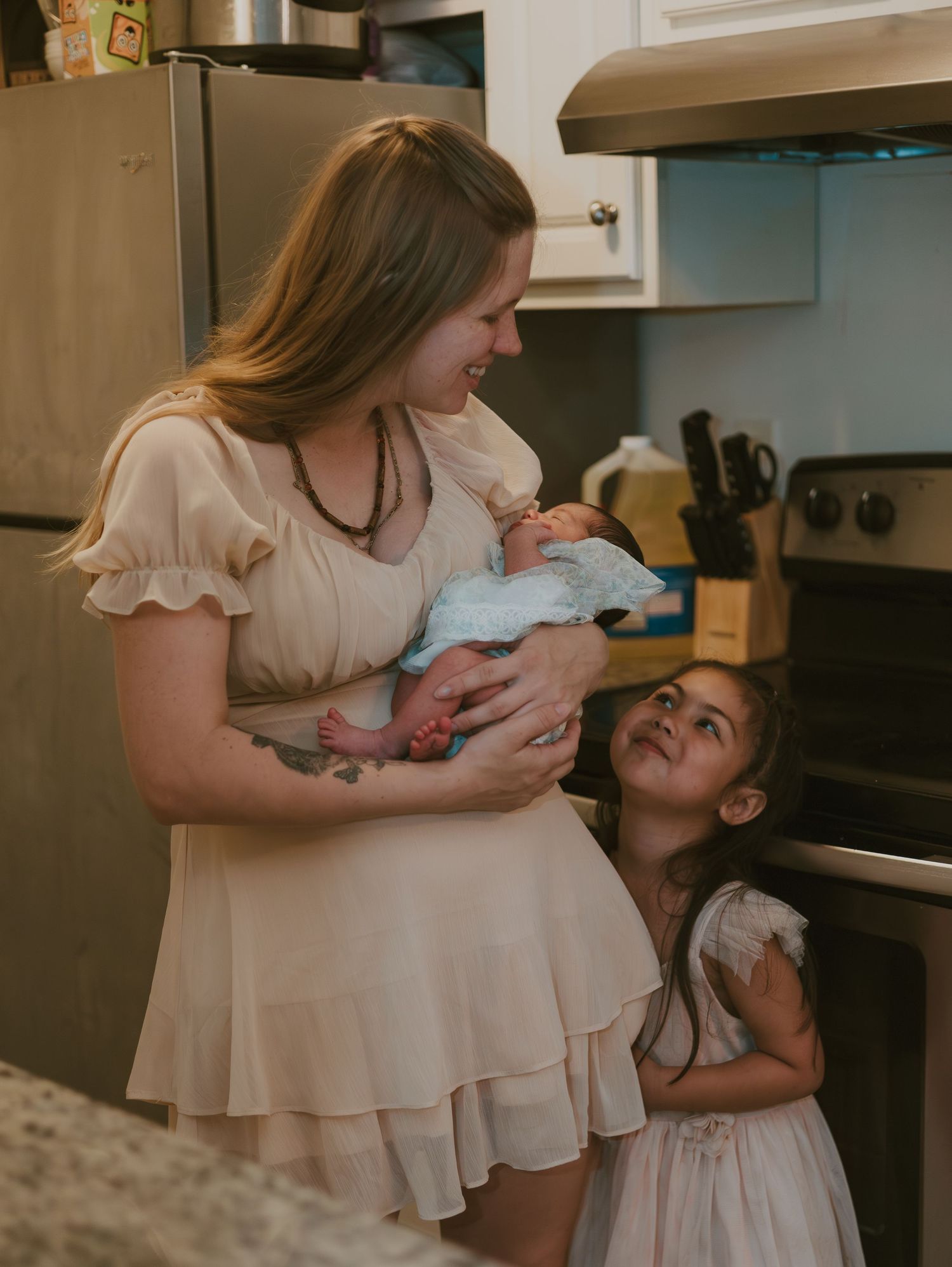 A mother in a beige dress shares tender moments with her young child in various candid poses in their kitchen.