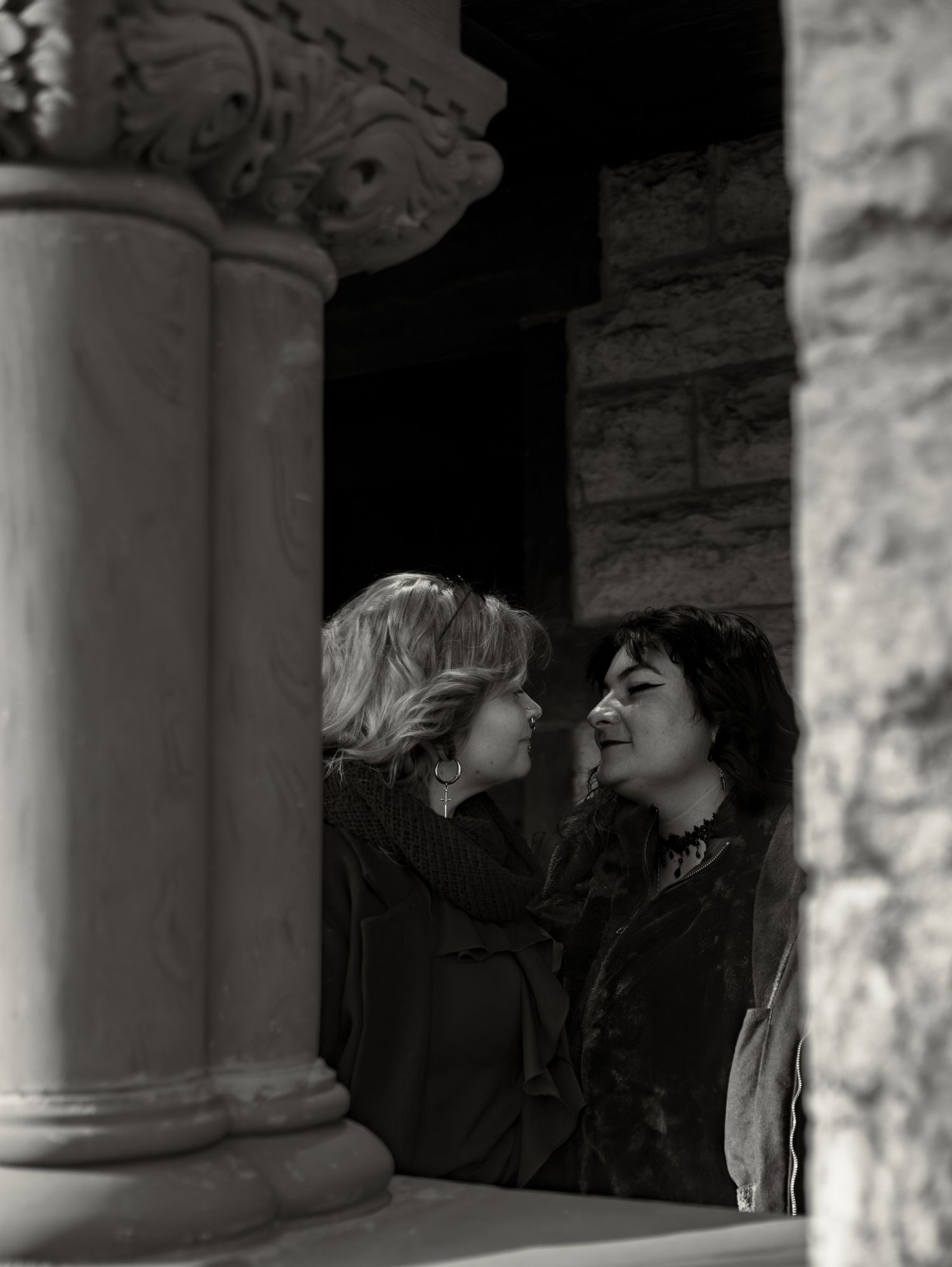 Two people share an intimate moment in black and white near ornate stone columns.