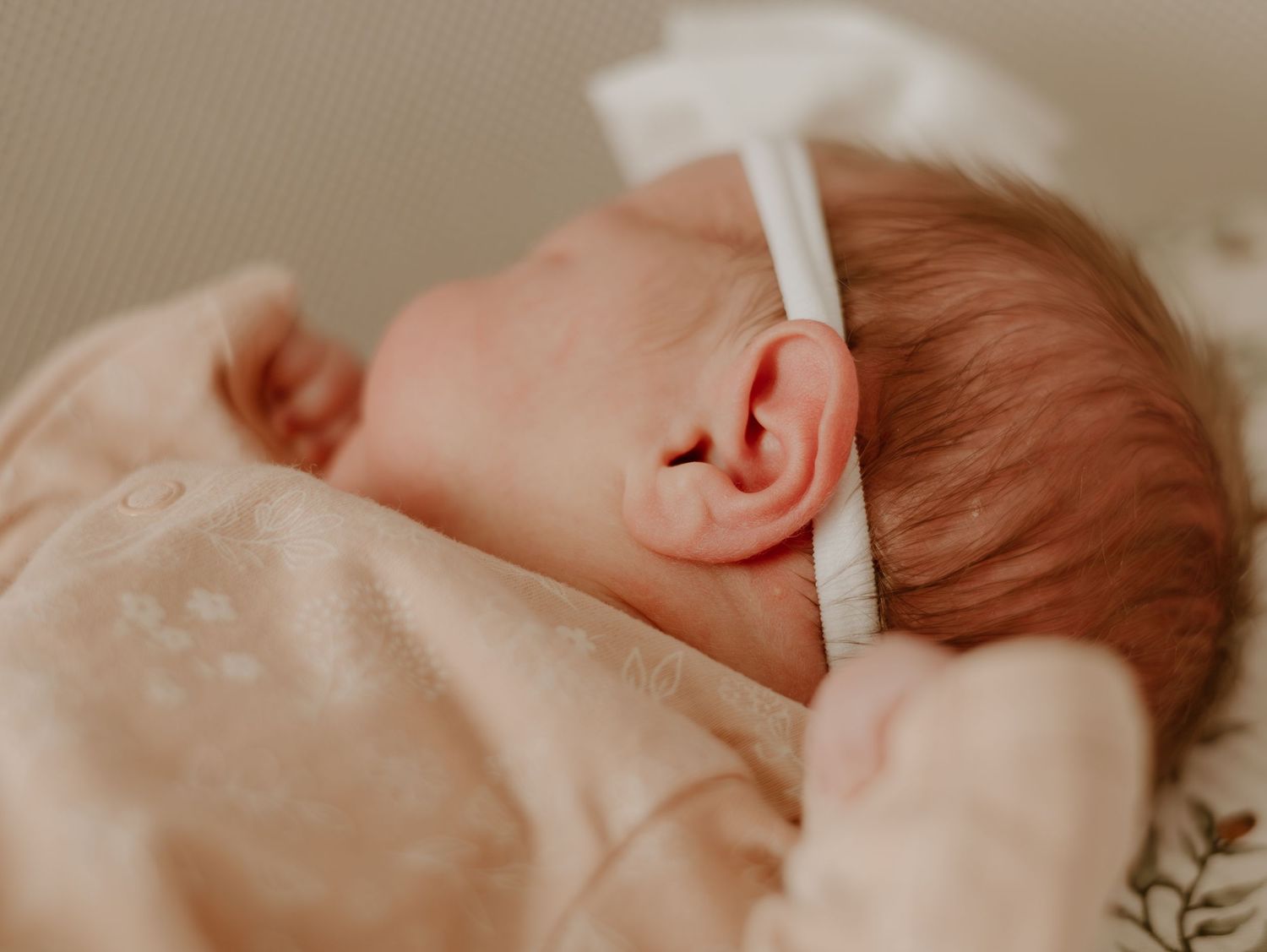 Close-up newborn photography with delicate details in warm beige and peachy tones.