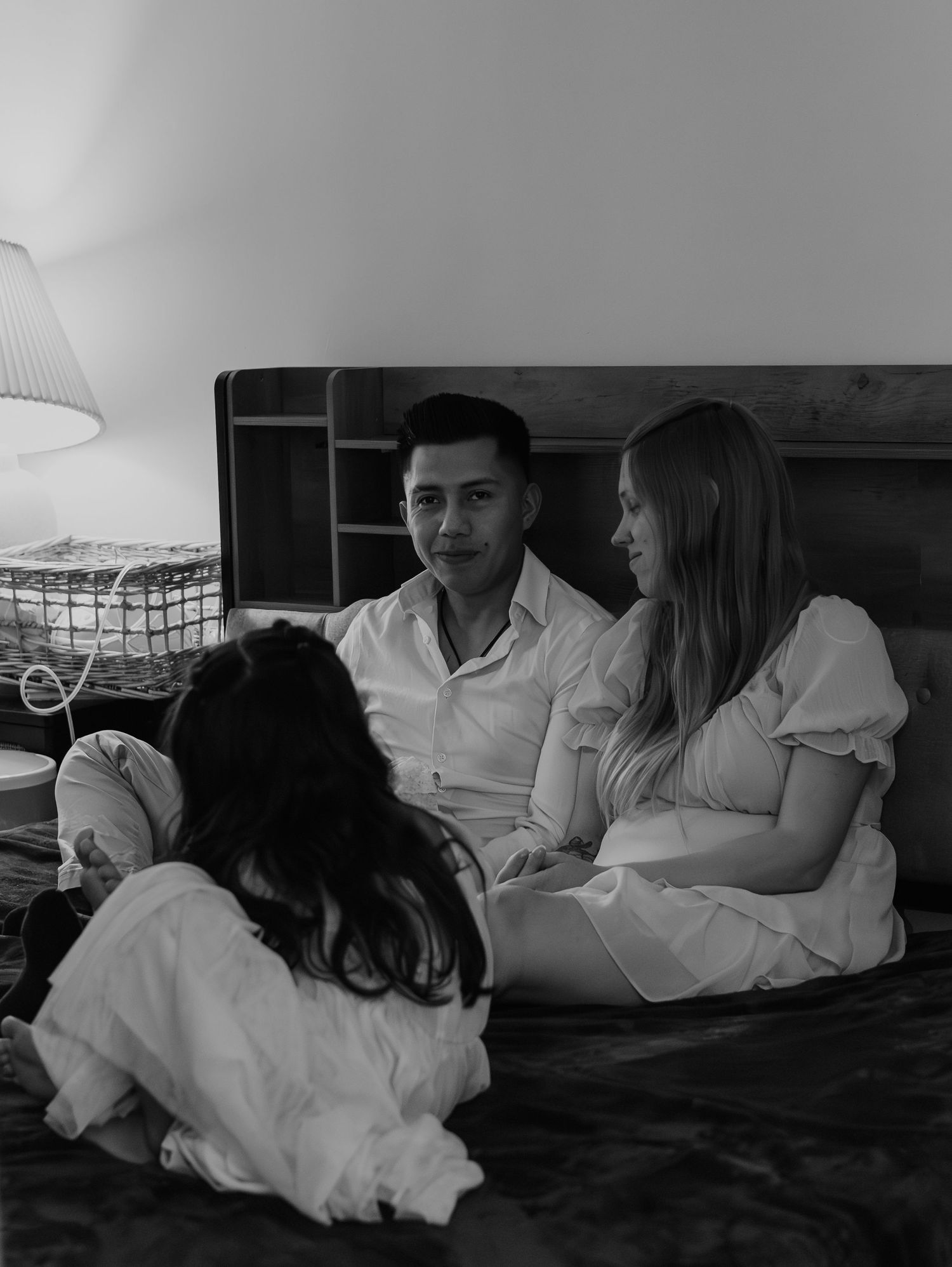 Family members lounge together on a bed in casual white clothing, captured in monochrome tones.