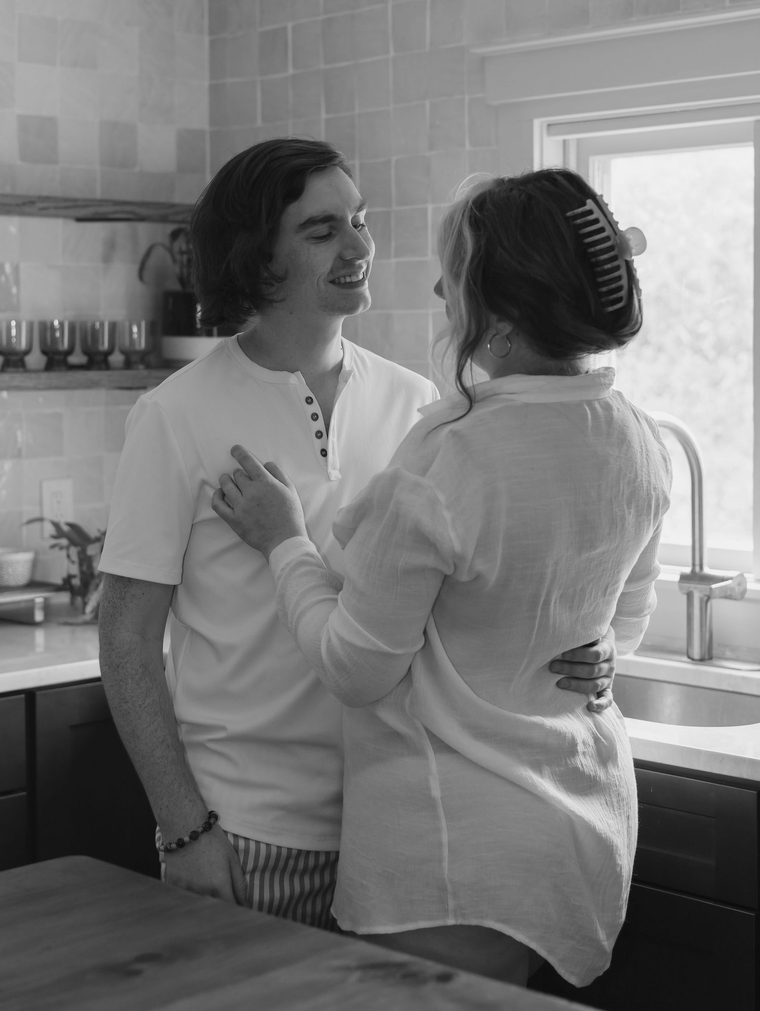 Black and white photo series showing two people in white clothing embracing in a kitchen setting.