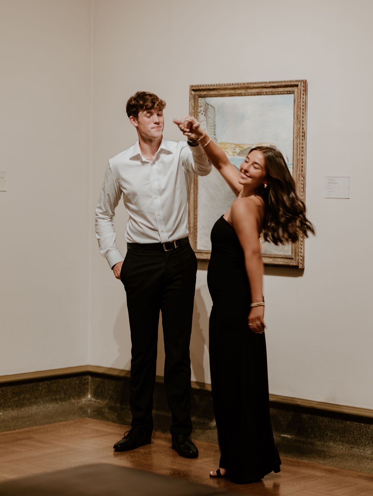 A couple dances together in an art gallery with framed paintings on display.