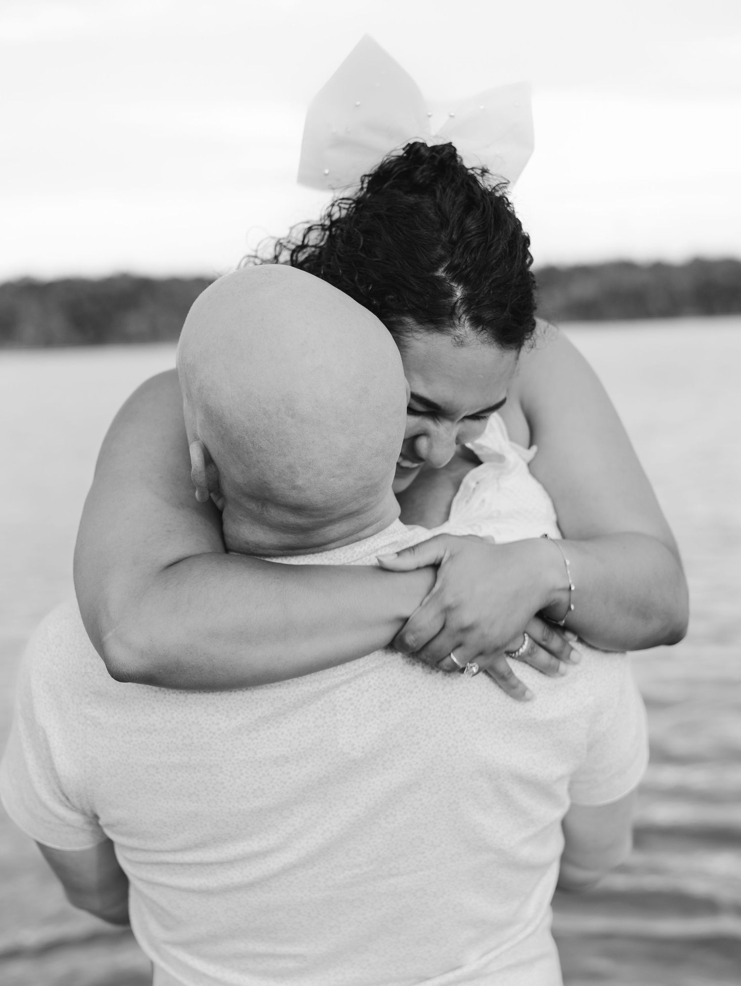 A tender black and white embrace captured by a lake, showing an intimate moment between two people.