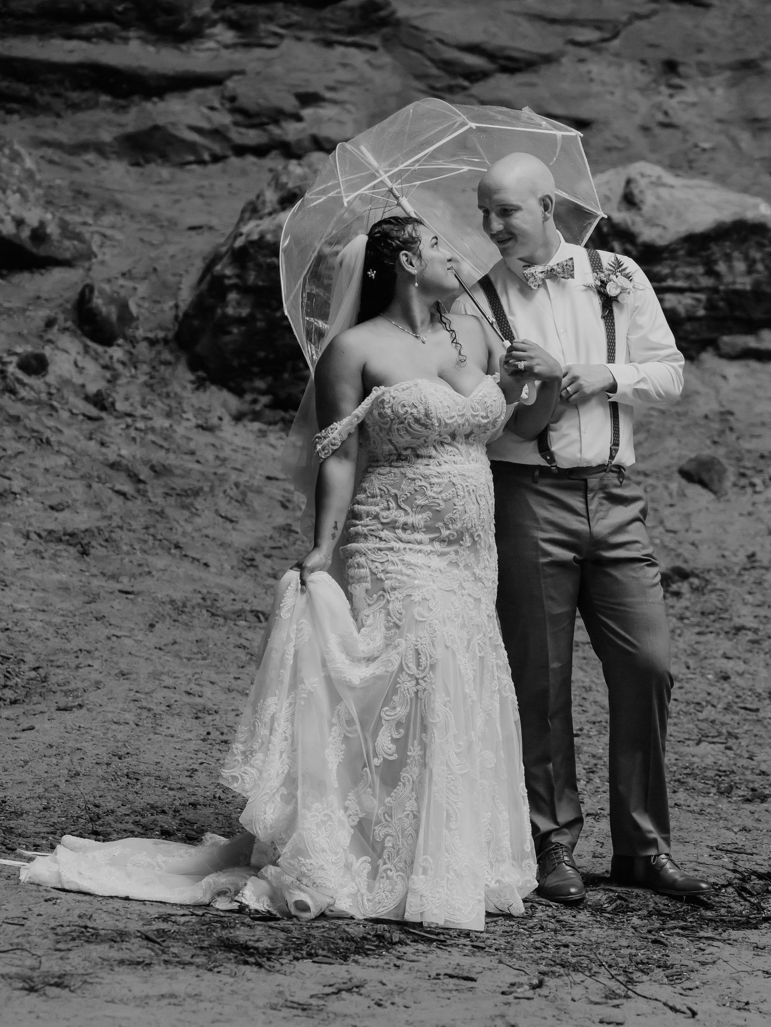 A couple poses in formal wedding attire against rocky beach terrain in a series of romantic black and white photos.