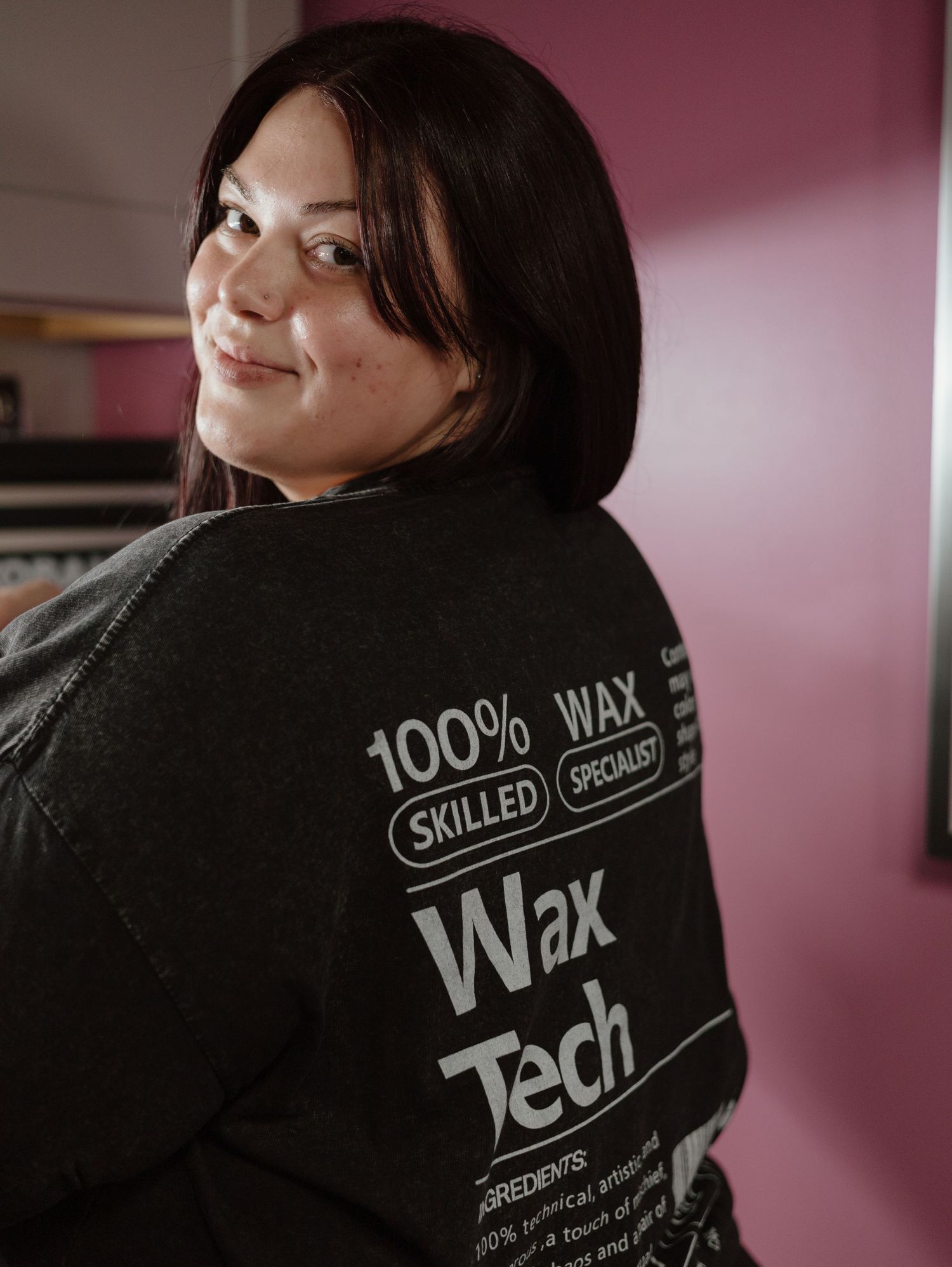 A cosmetology professional in a black uniform displaying text that reads Wax Tech.