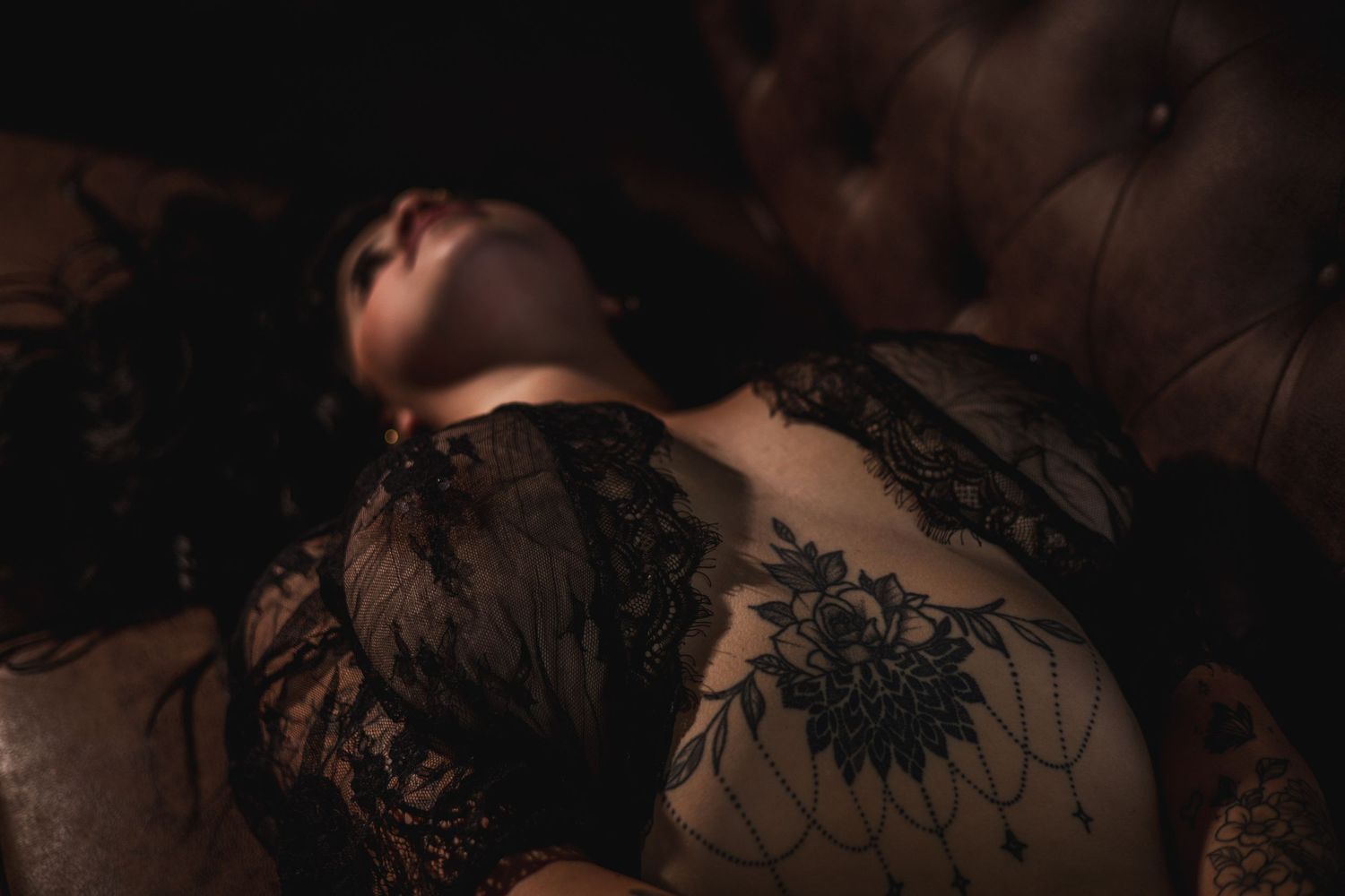 Dark lace boudoir photo with dramatic lighting on leather furniture.