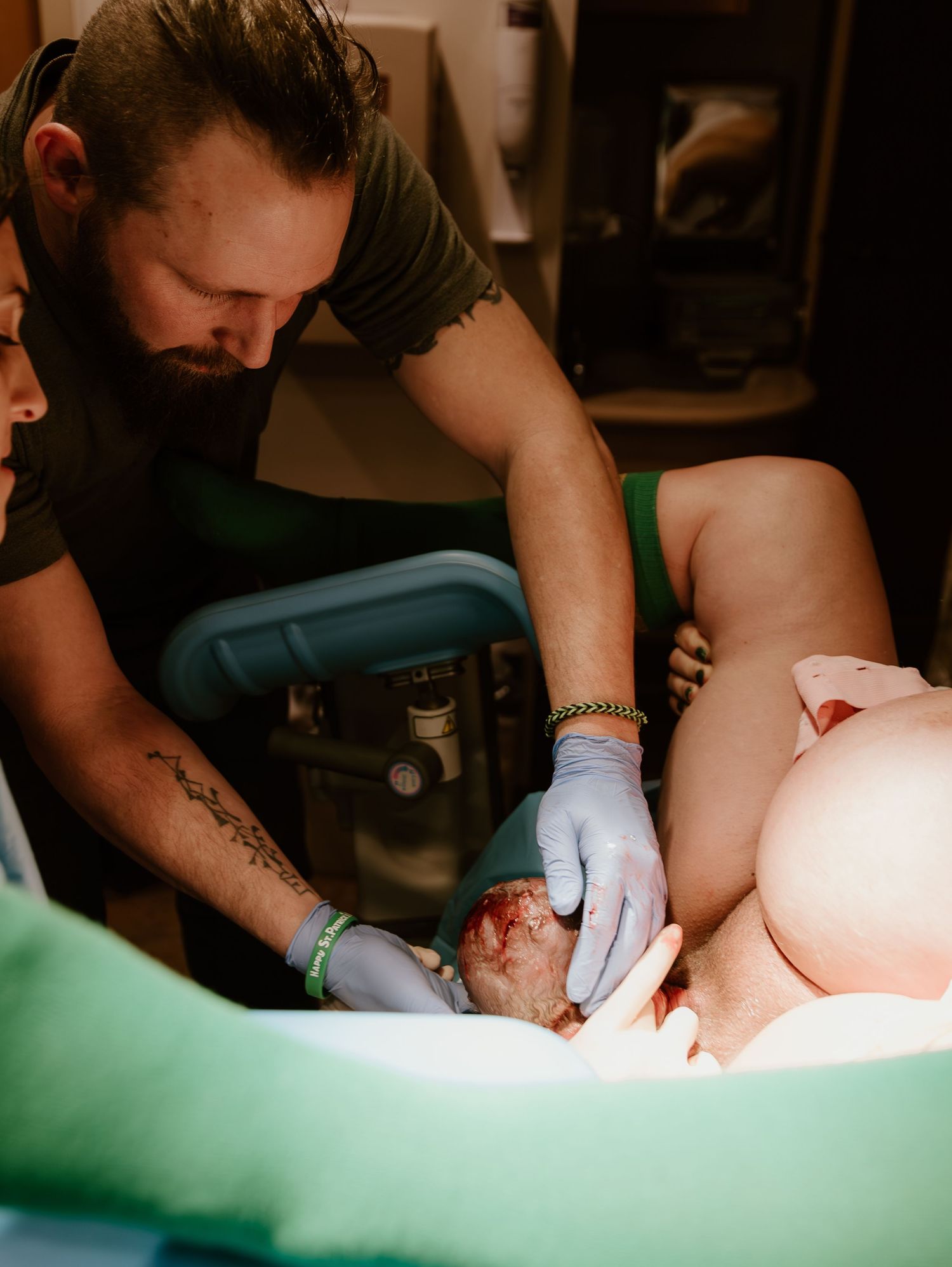 Medical professional in blue gloves assists during childbirth in a dimly lit birthing room.