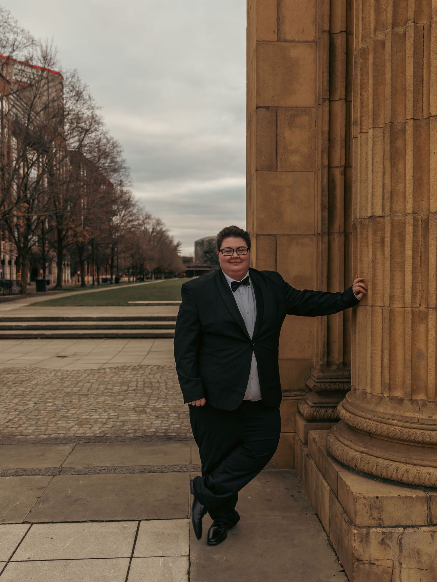 Groomsman poses playfully against stone column in formal wear.