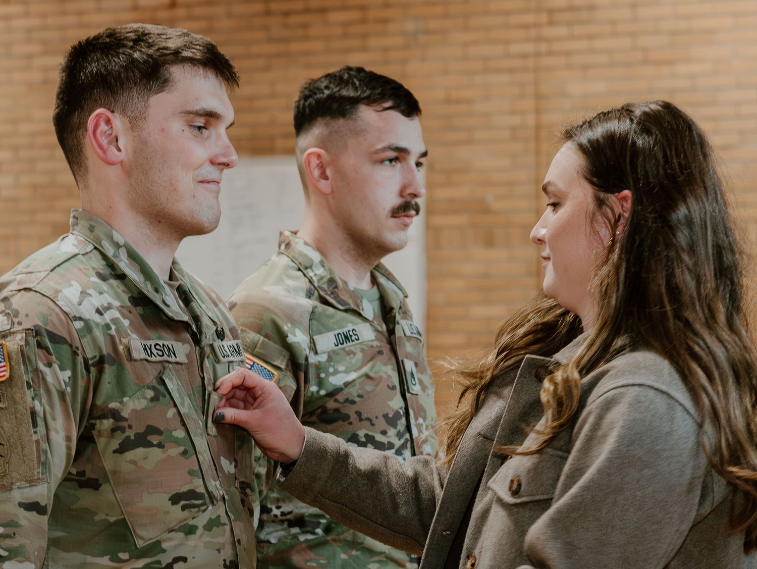Two military service members in camouflage uniforms having a conversation with a woman in a grey sweater.