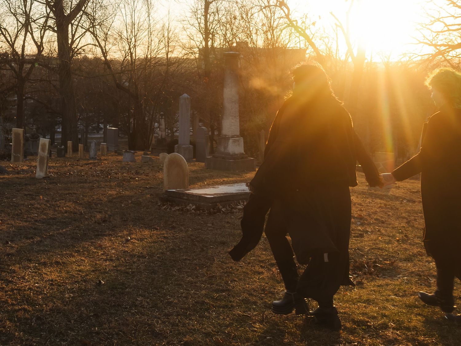 Warm sunset light illuminates a cemetery scene with dark figures and headstones creating dramatic silhouettes.