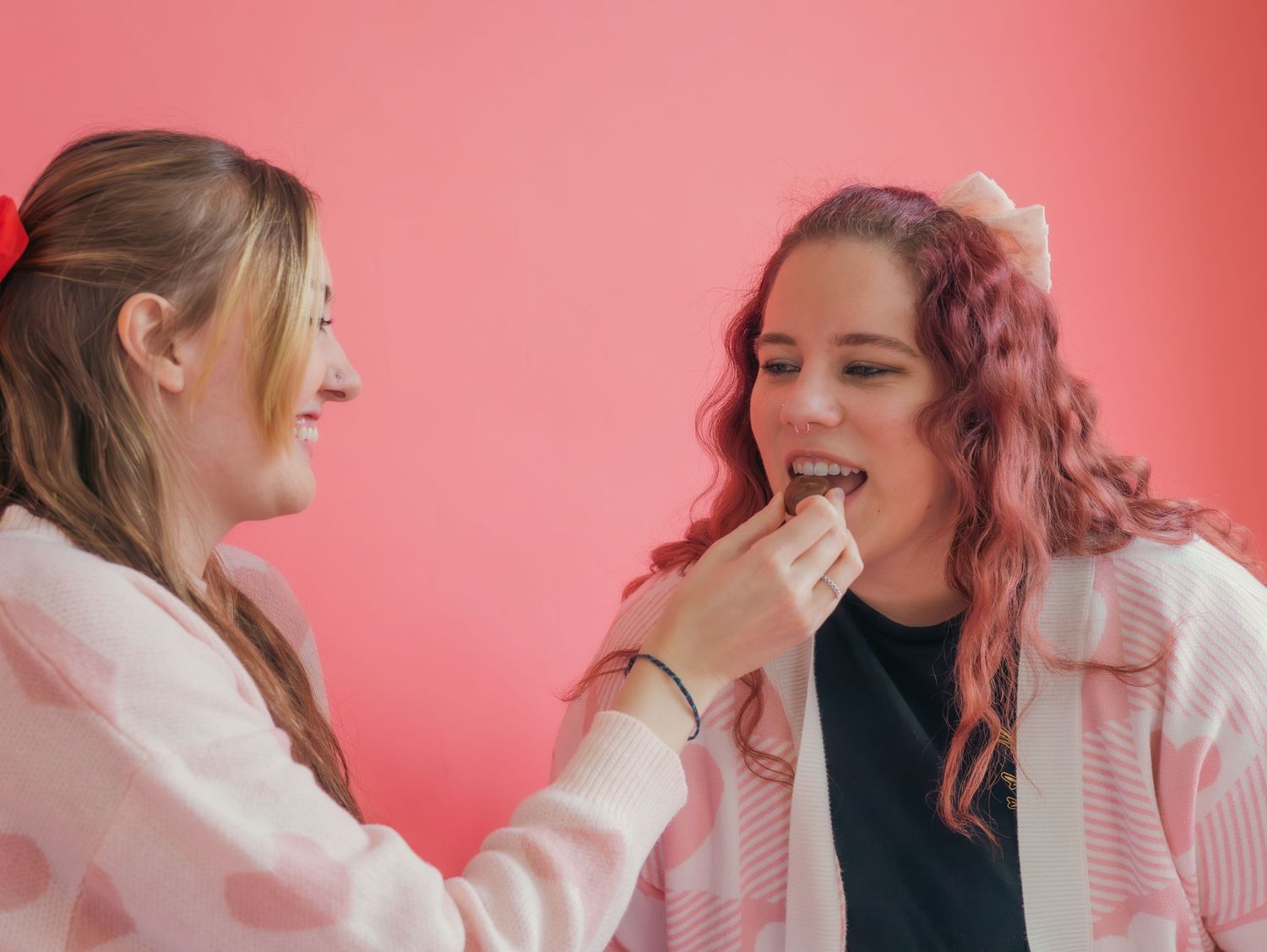 Friends sharing sweets and laughter against a pink backdrop.