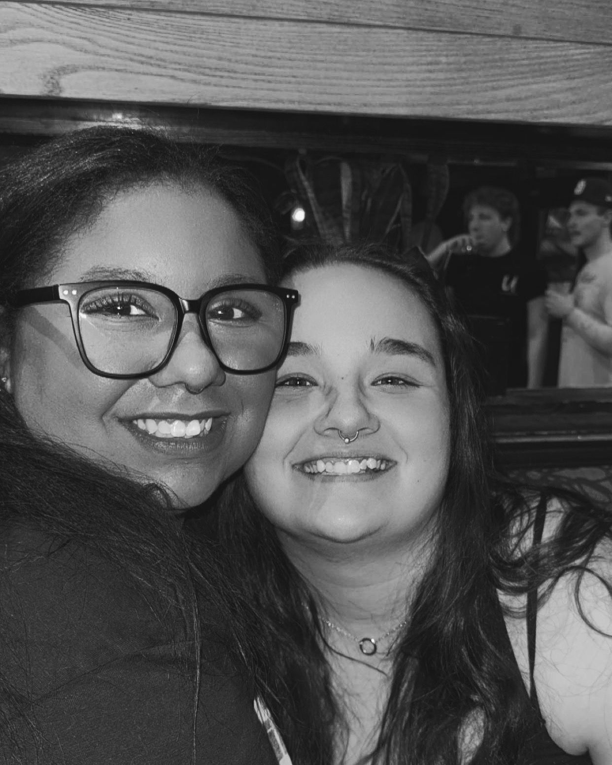 Two friends smiling together in a black and white photo at a social gathering.