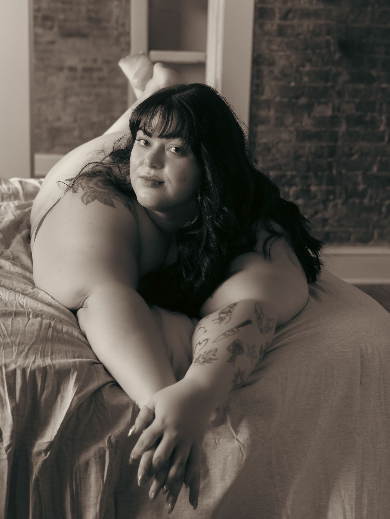 Monochromatic portrait against exposed brick wall in natural window light.