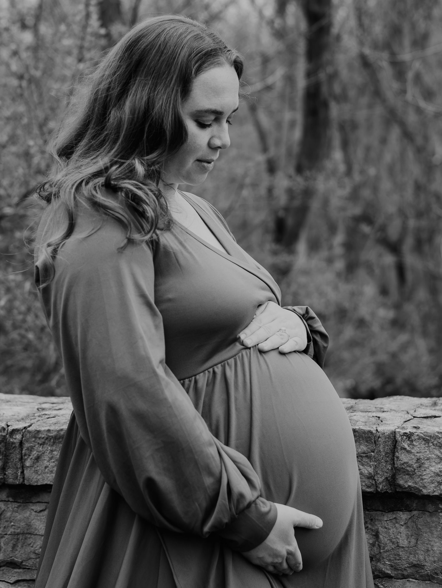 Black and white outdoor maternity photoshoot series showing embrace of pregnant belly in natural wooded setting.