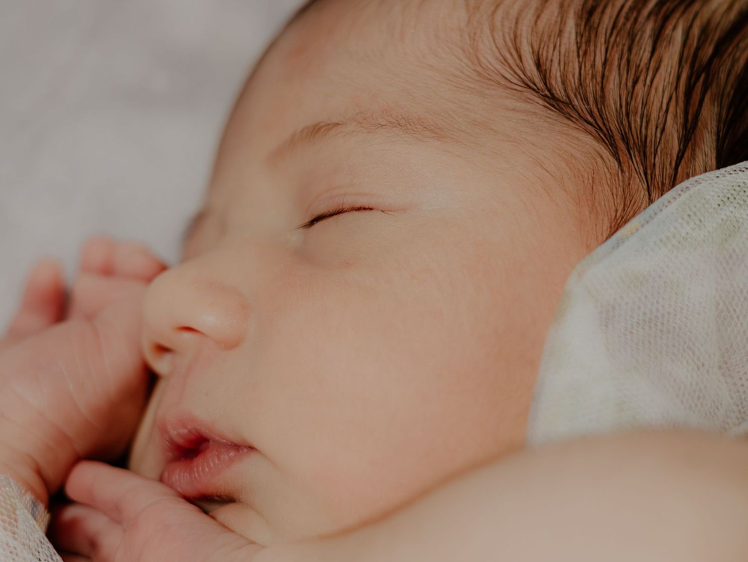 A sleeping newborn baby rests peacefully in soft light, with closed eyes and delicate features.