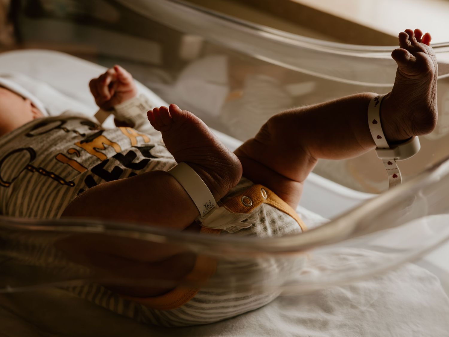 Small feet in patterned socks and sneakers resting on white sheets in warm lighting.