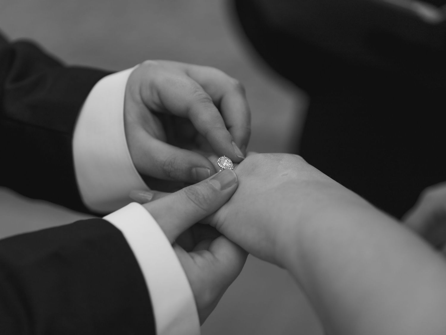 Black and white close-up of hands exchanging wedding rings during ceremony.