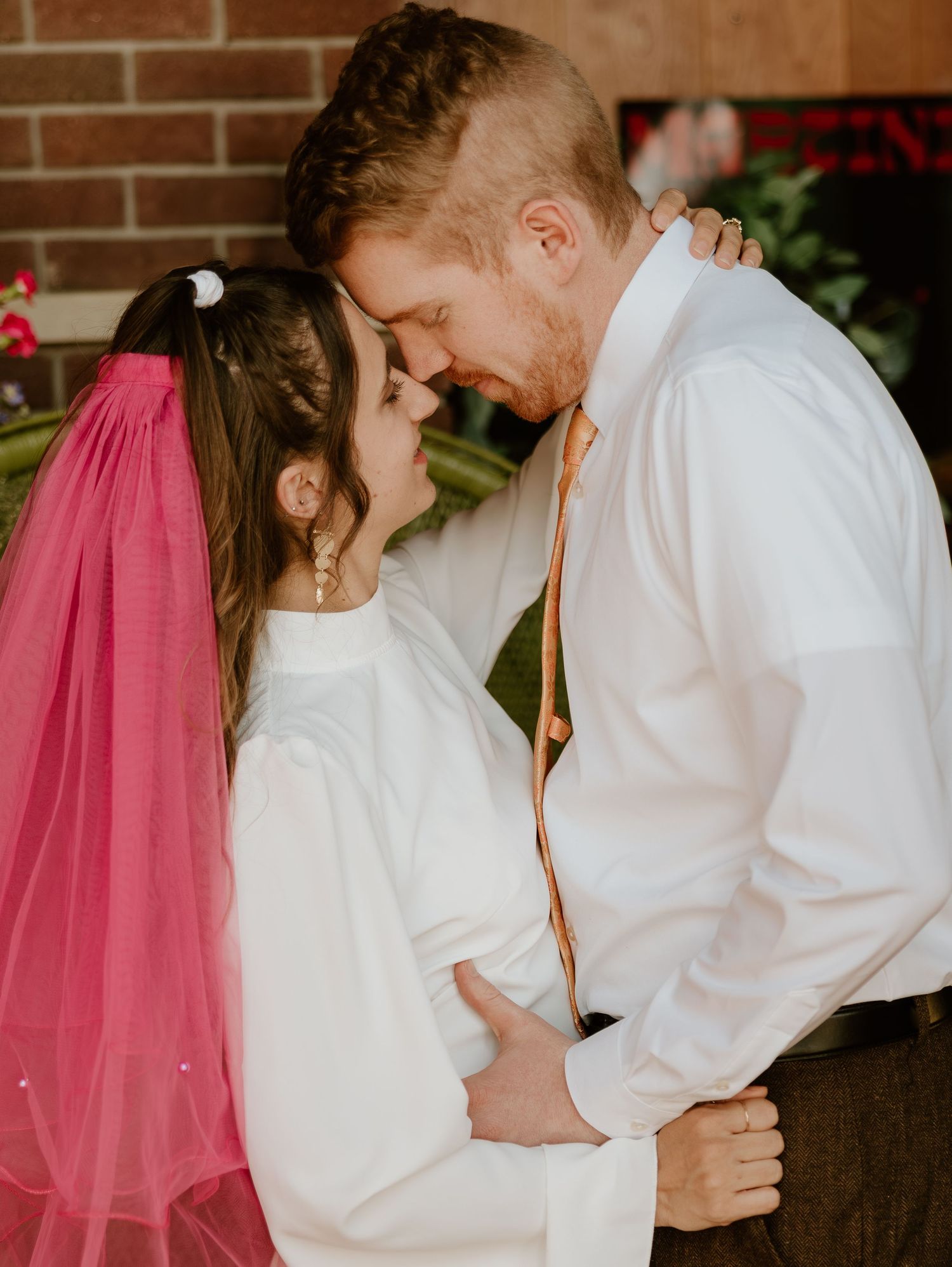 A romantic wedding photo shows a couple sharing an intimate moment together against a brick wall background.