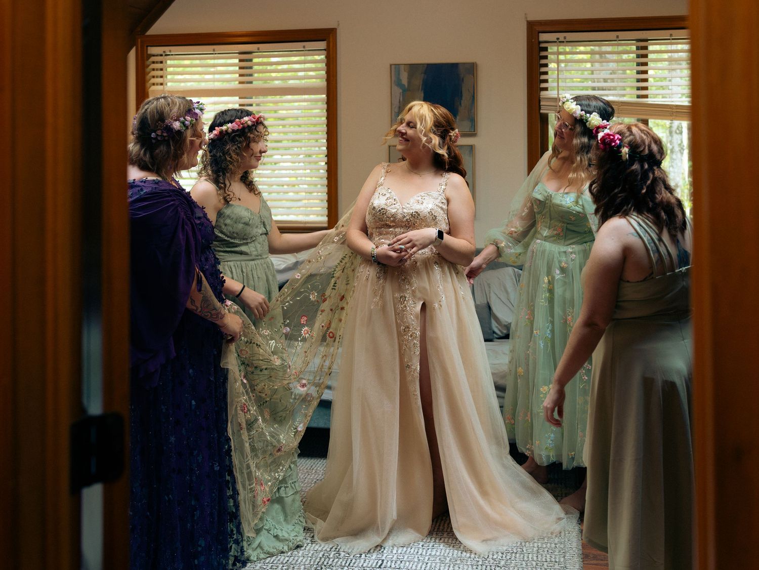 A group in formal attire gathers in a room with window light, wearing elegant dresses in shades of blue and champagne.