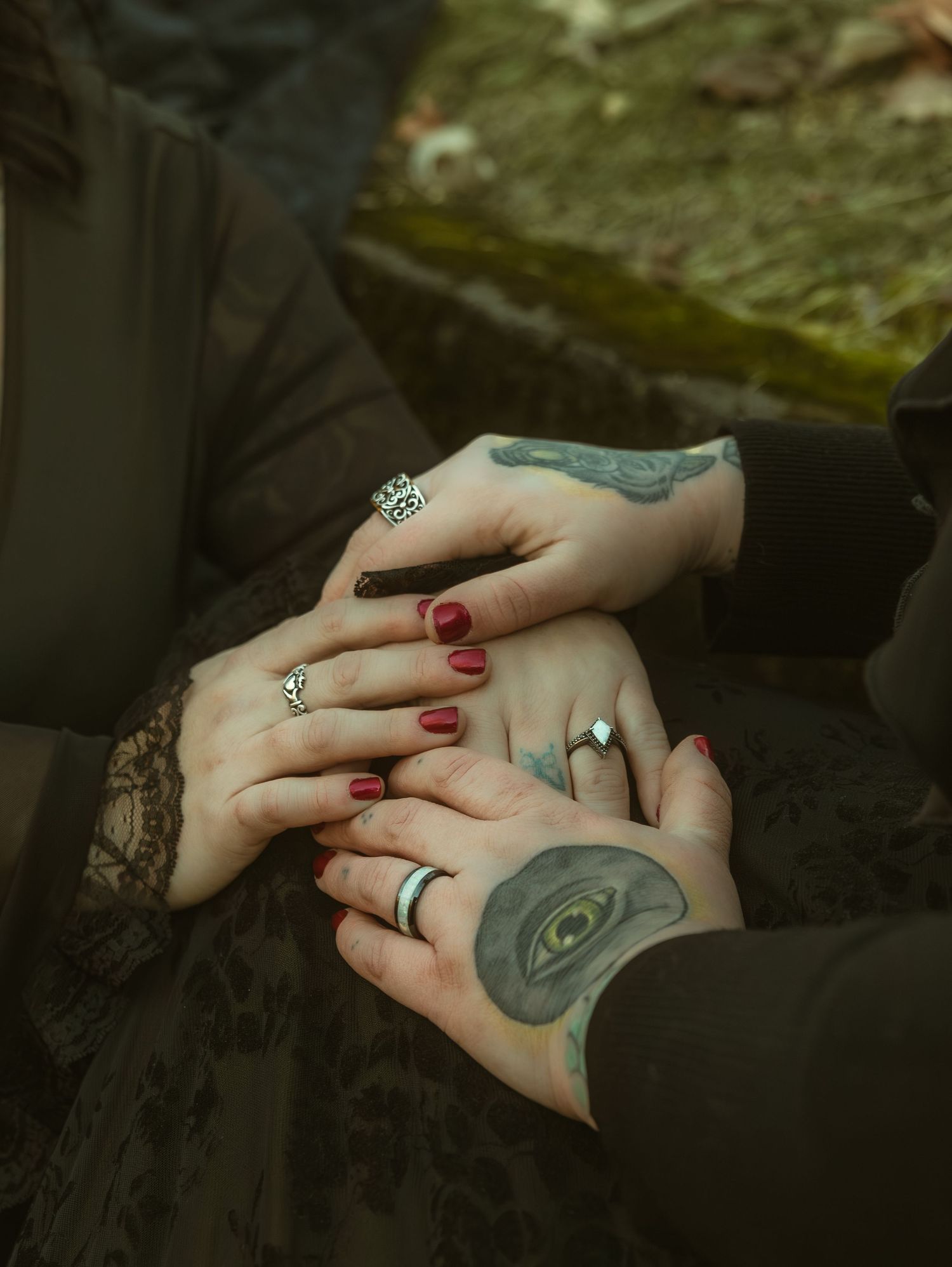 Close-up of hands with rings and tattoos intertwined against a dark background.