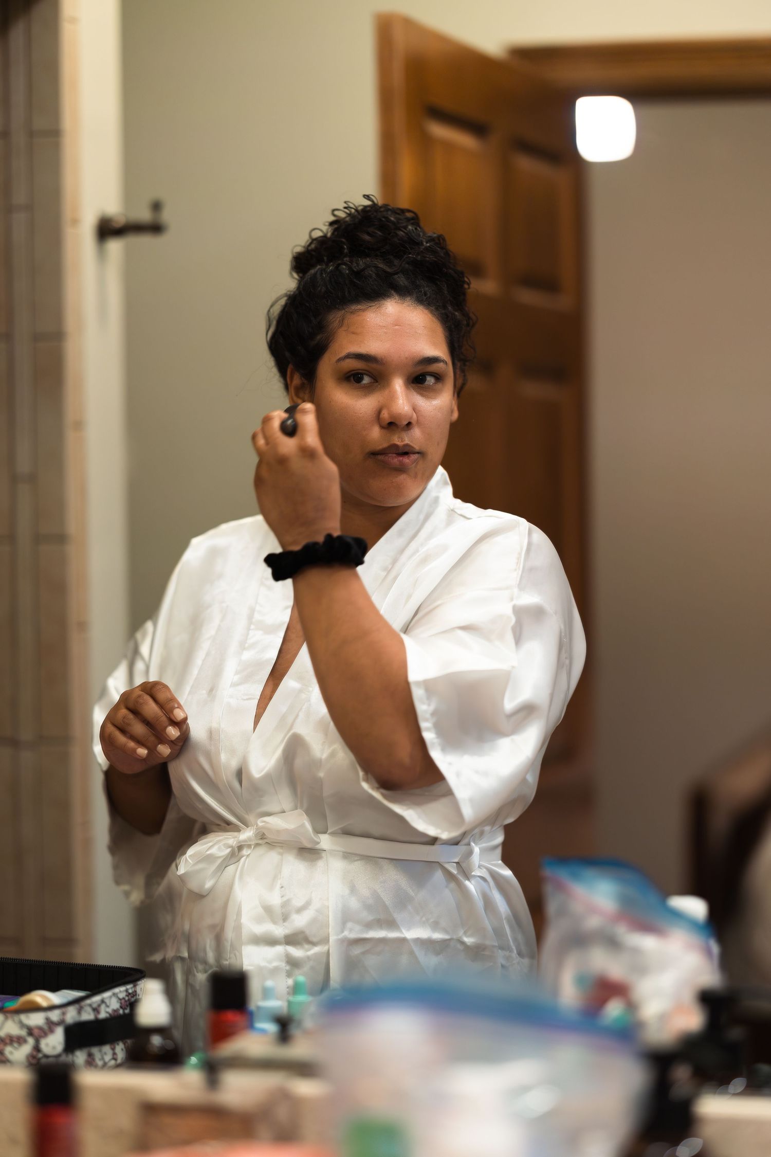 Someone in a white robe applies makeup while getting ready in front of a bathroom counter.