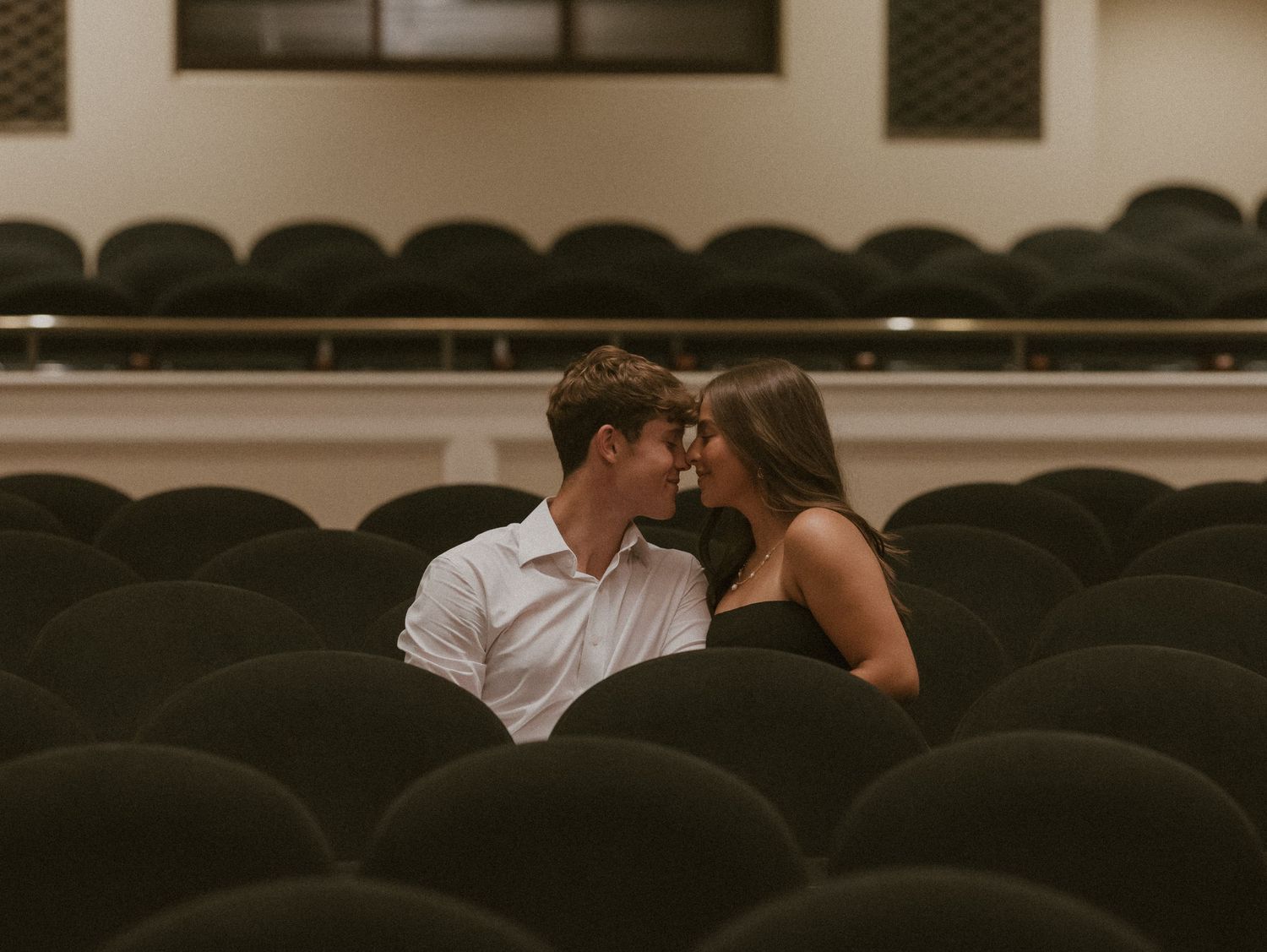 A couple shares an intimate moment while sitting in dark theater seats during a movie.