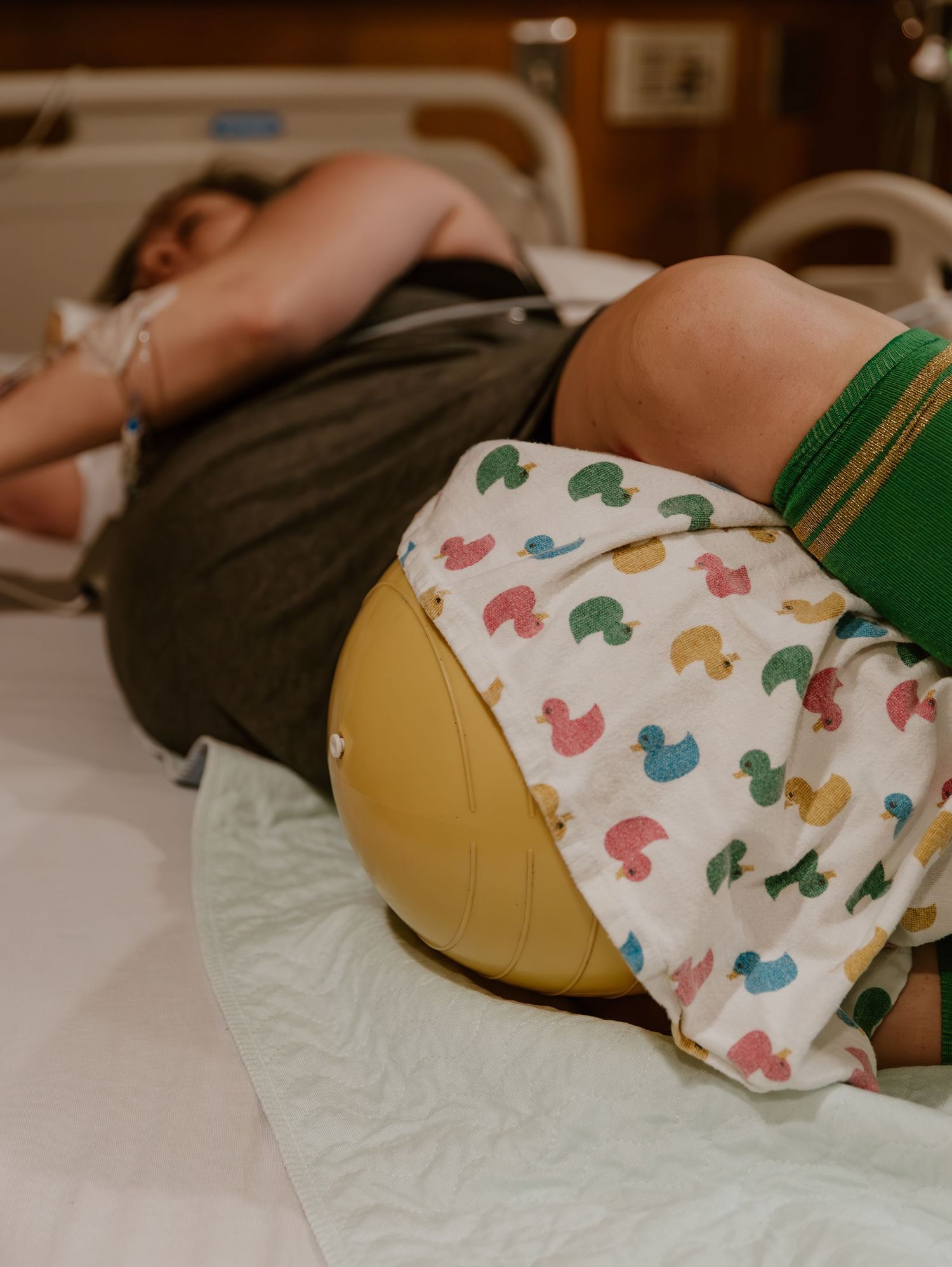 Baby wearing a white diaper with colorful duck patterns lies on a hospital bed under medical care.